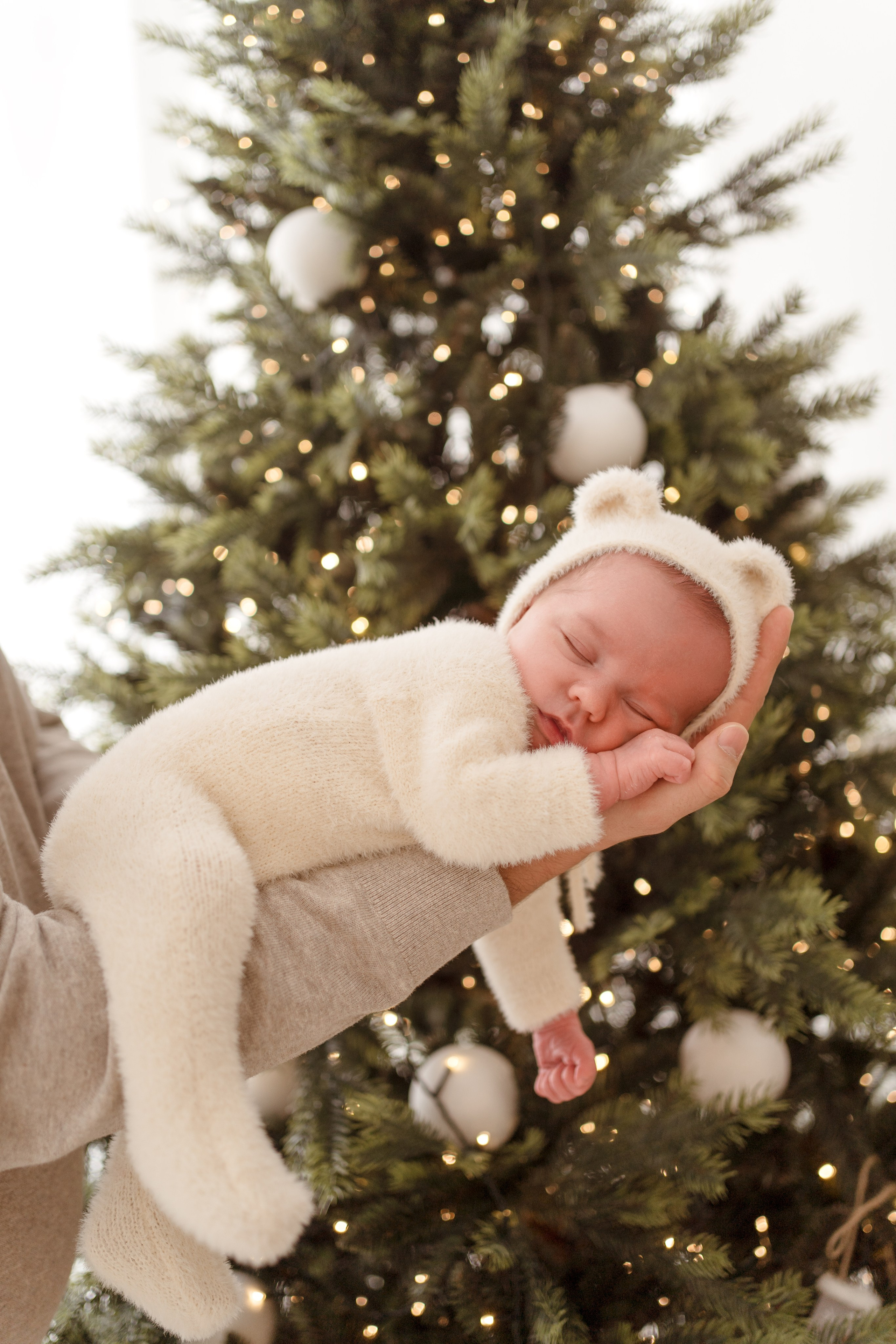 Sesja noworodkowa w świątecznym wydaniu. Noworodek w stroju misia na tle choinki.