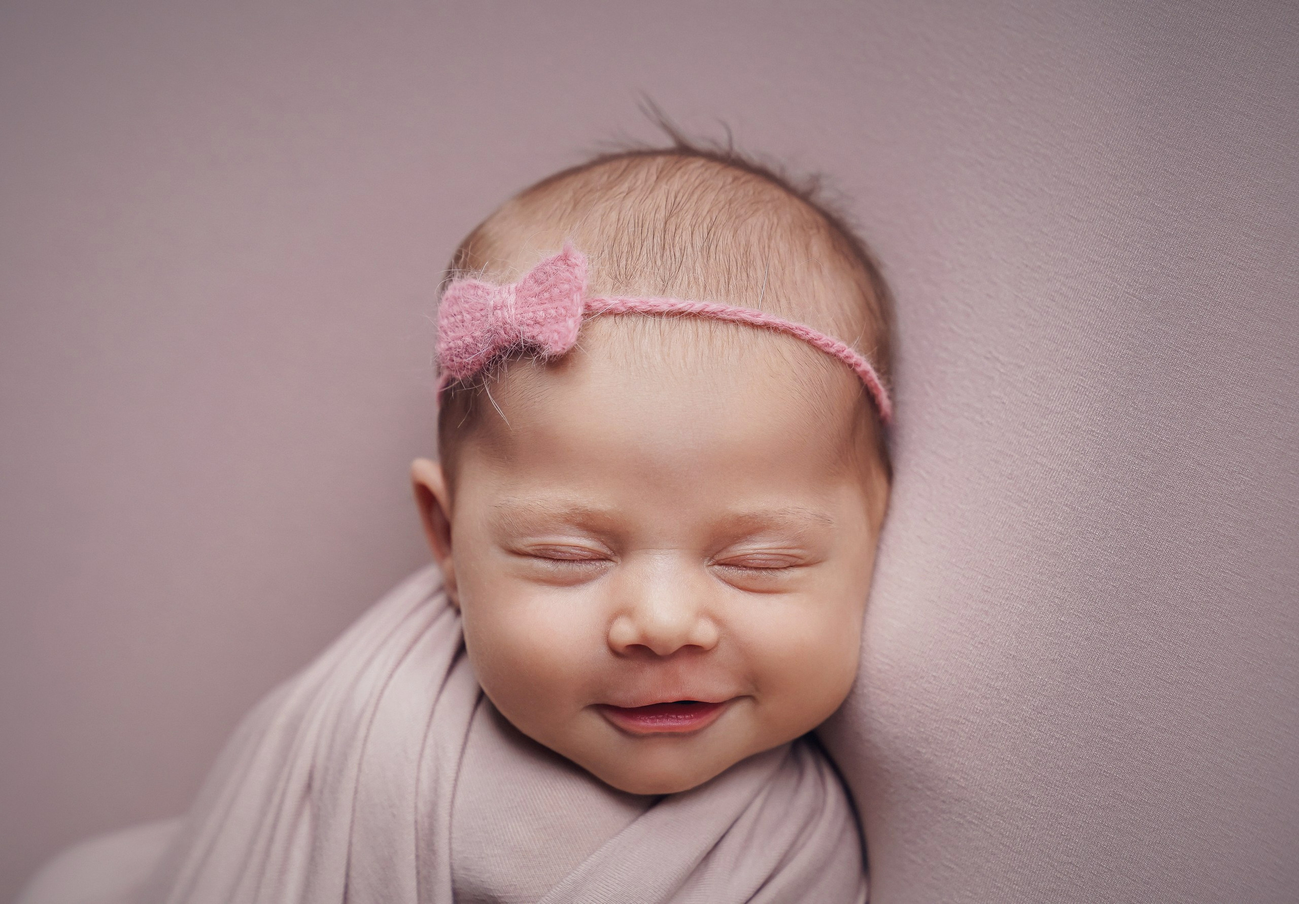 Sleeping newborn baby girl smiling in cozy wrap