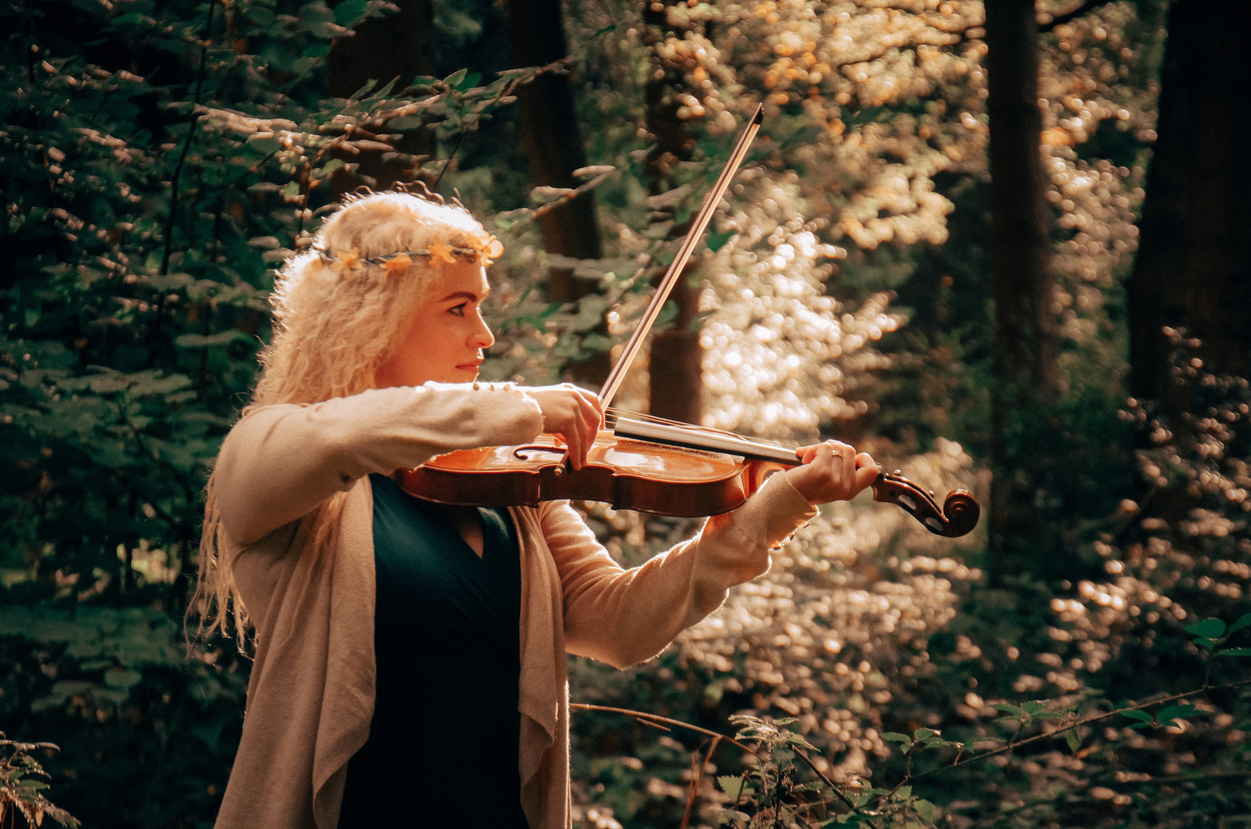 Woman playing the violin in a sunlit woodland during an Artistic Discovery Session in Solihull.