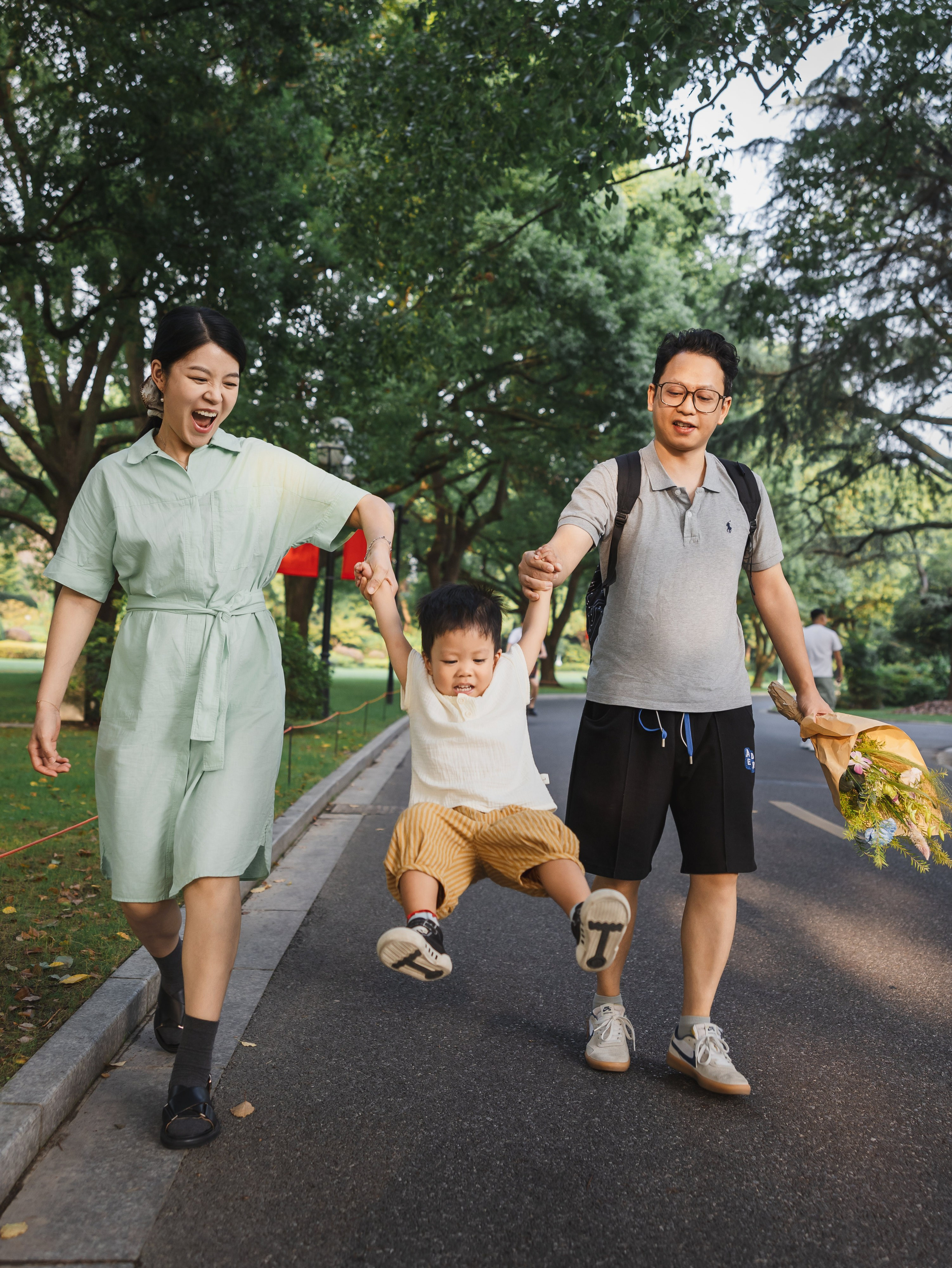 A Shanghai family walks through a park while lifting their toddler between them in a natural documentary moment.