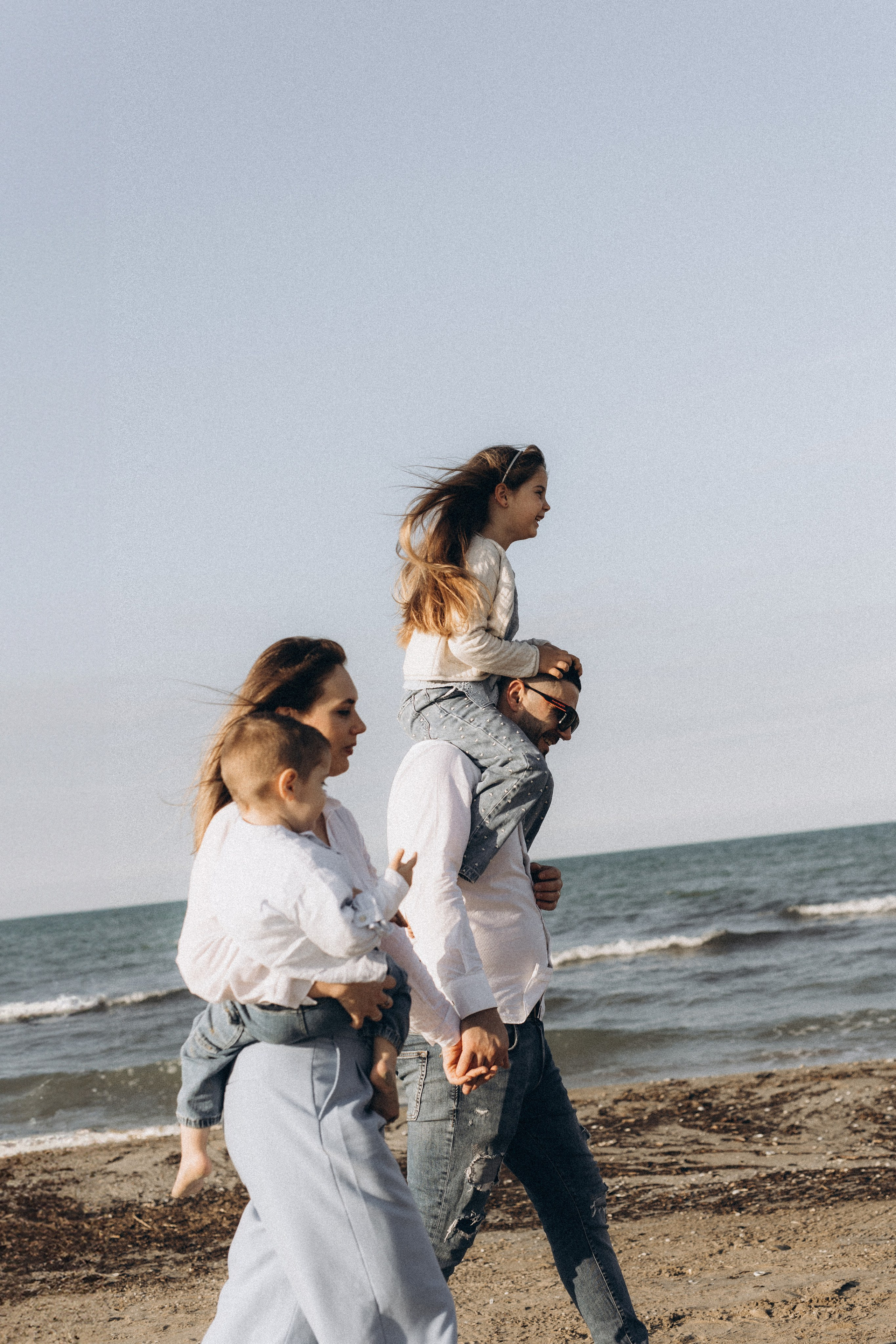 Famiglia che cammina lungo la spiaggia di Riccione con i bambini. Movimento naturale, vento leggero e atmosfera estiva. Fotografia di famiglia spontanea sulla costa italiana.