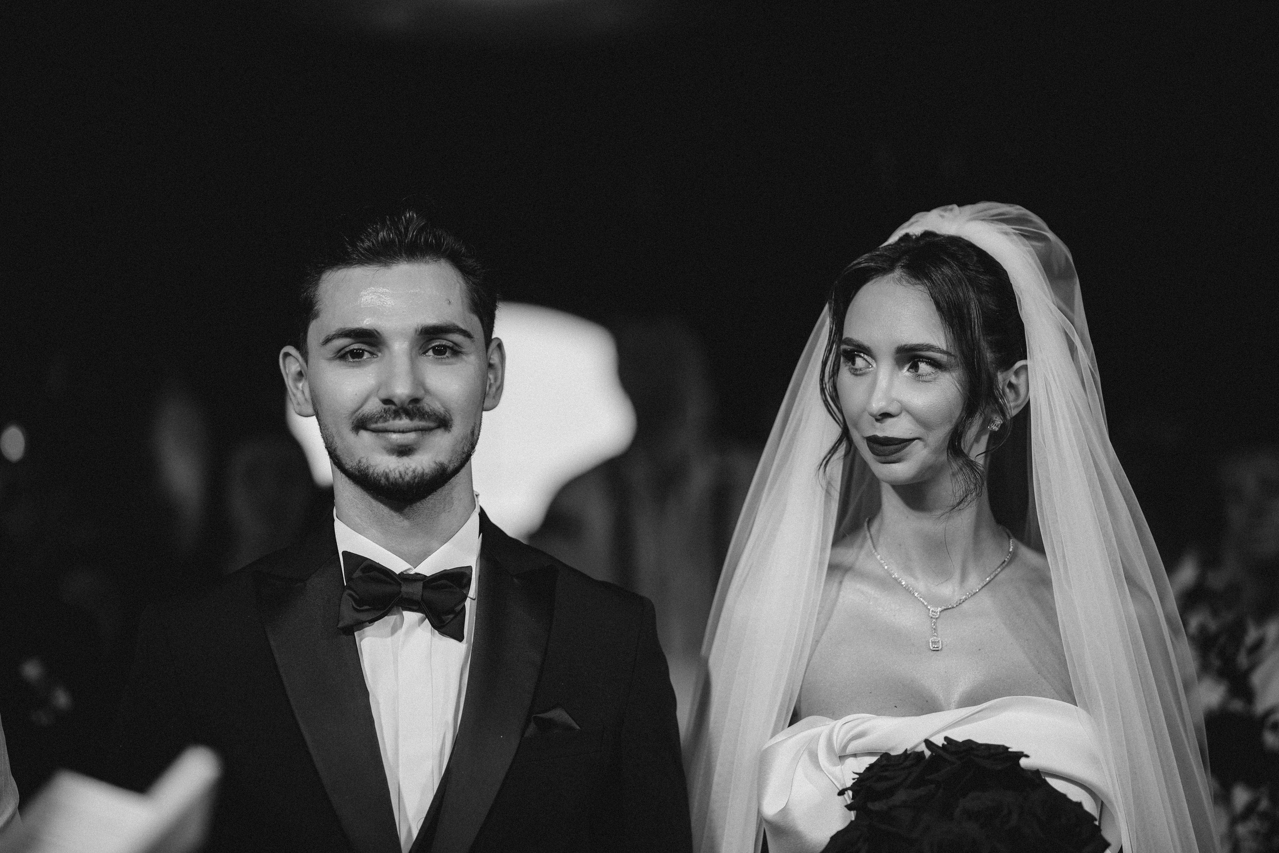 Fotografie alb-negru cu mirii ținându-se de mână în timpul slujbei.