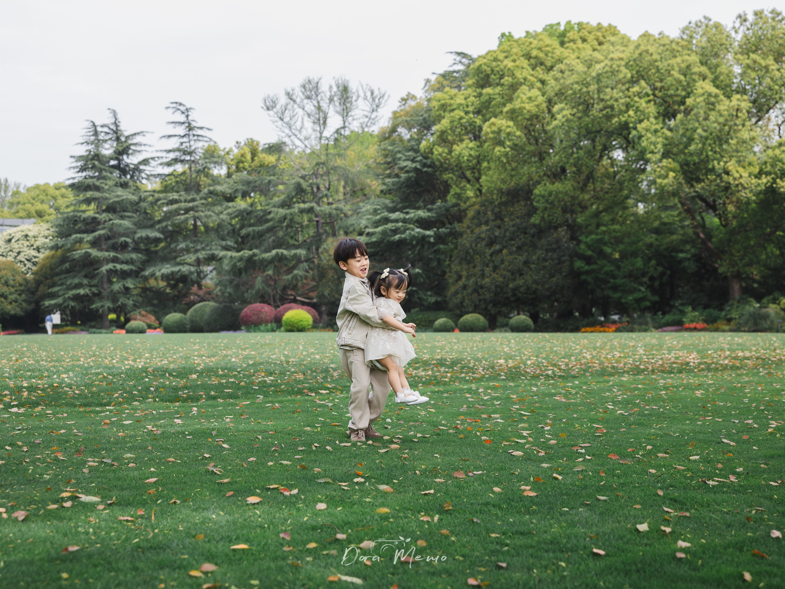 An older brother picks up his little sister on the grass, both grinning