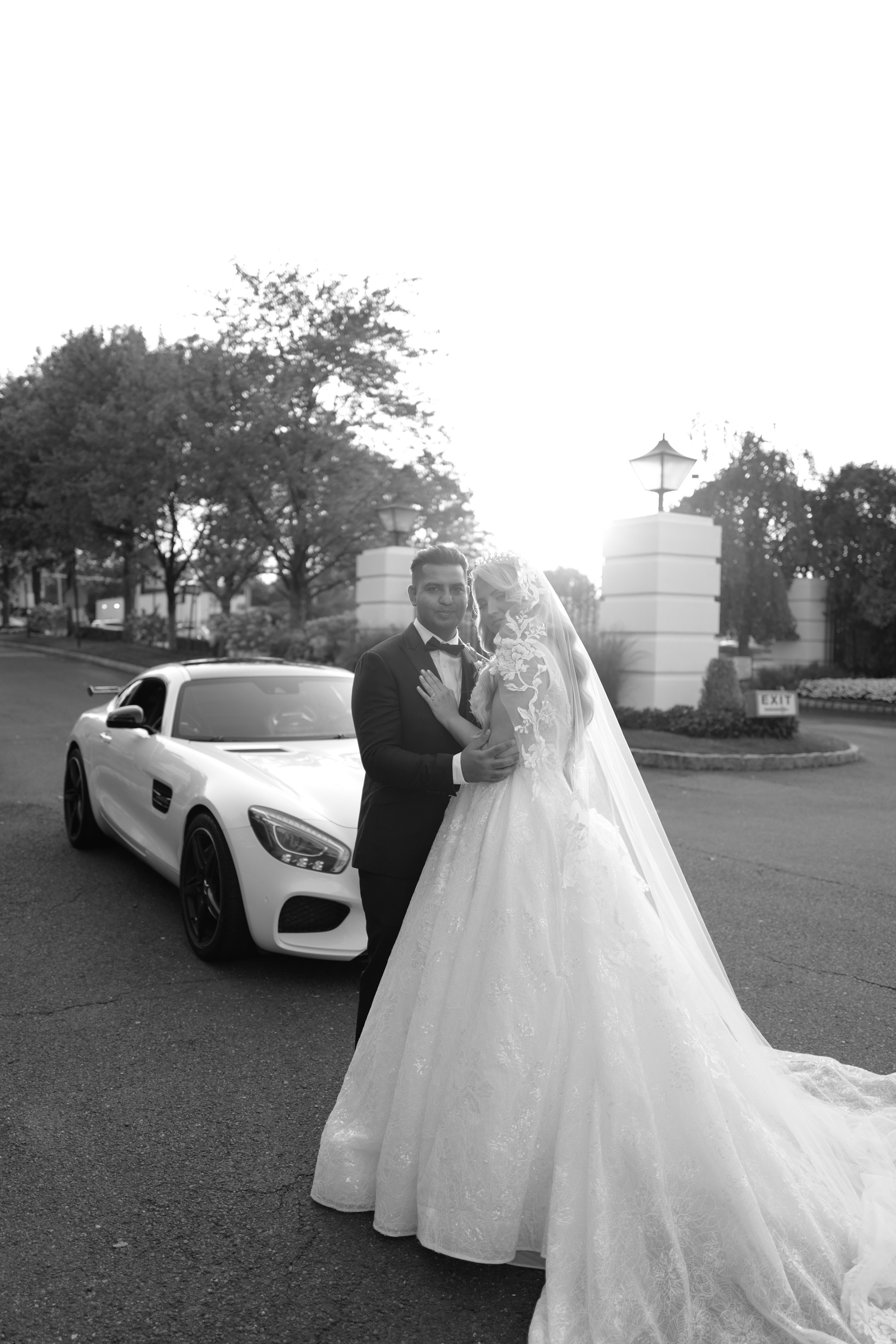 a bride and groom pose for a photo in front of their car