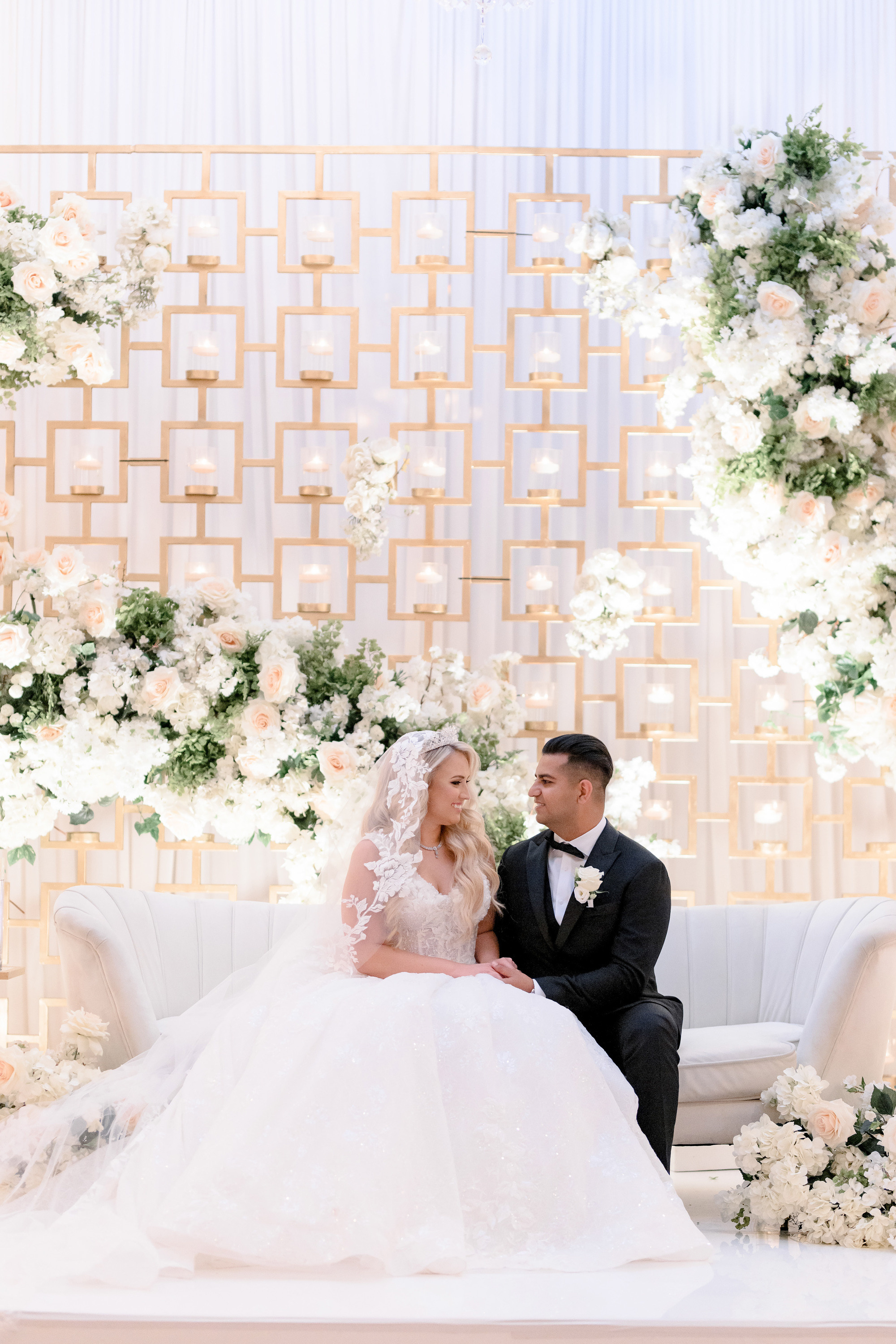 a bride and groom sitting on a couch in front of a floral wall