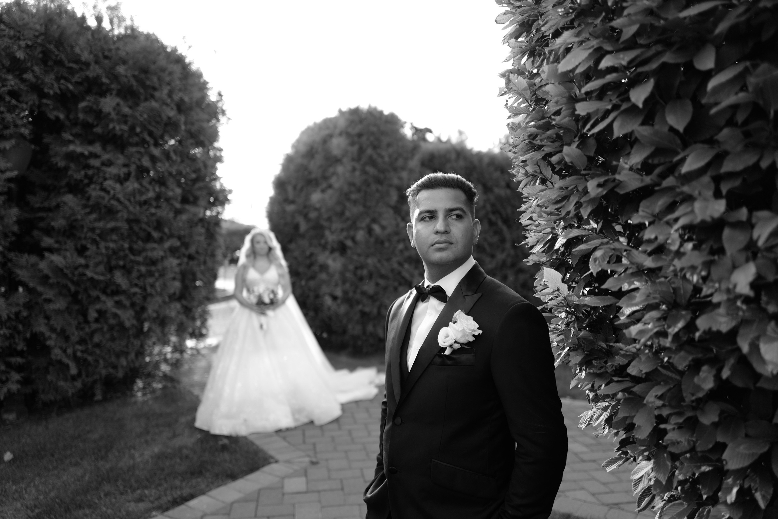 a man in a suit and tie standing next to a hedge