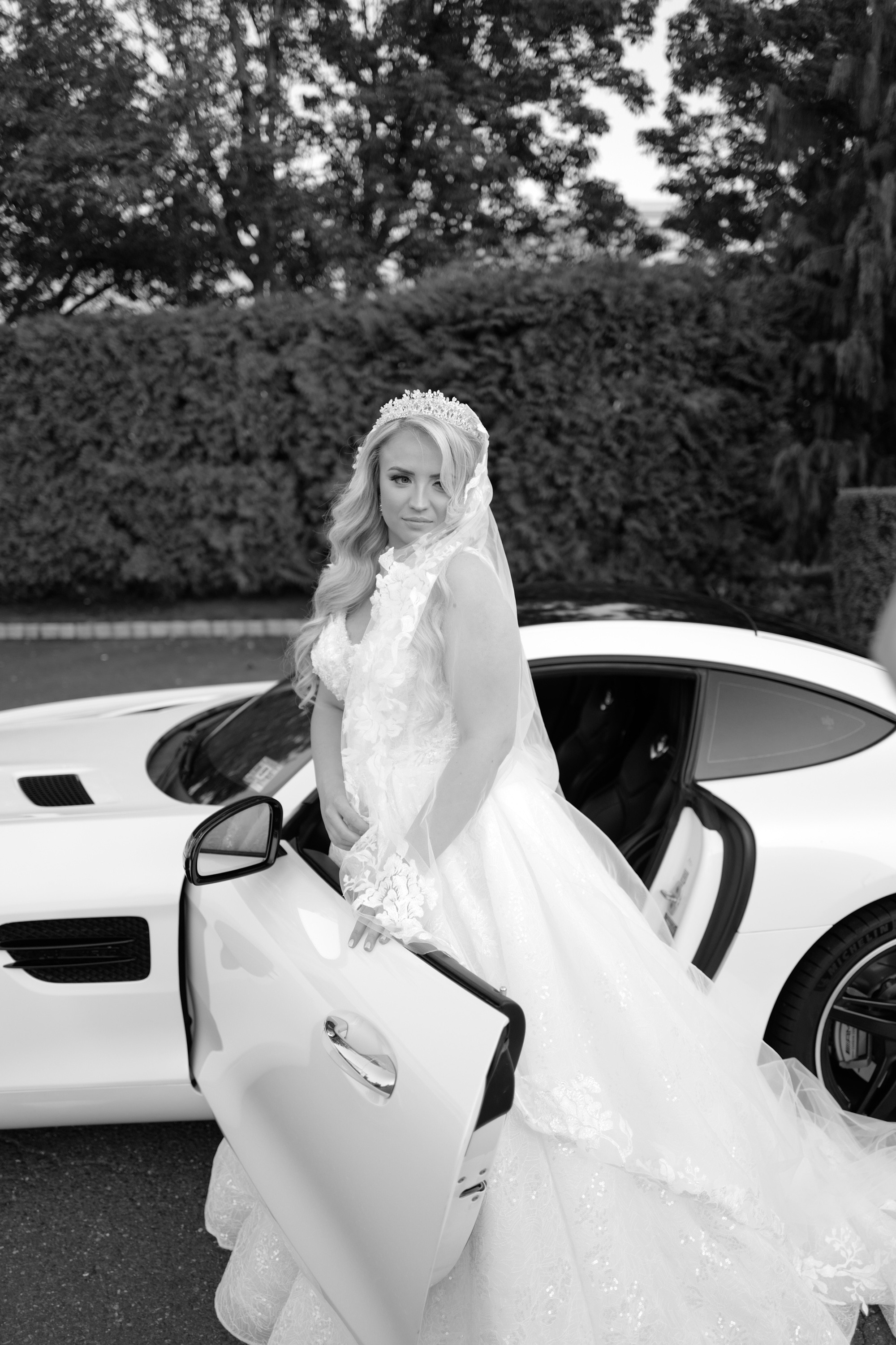 a woman in a wedding dress standing next to a white car