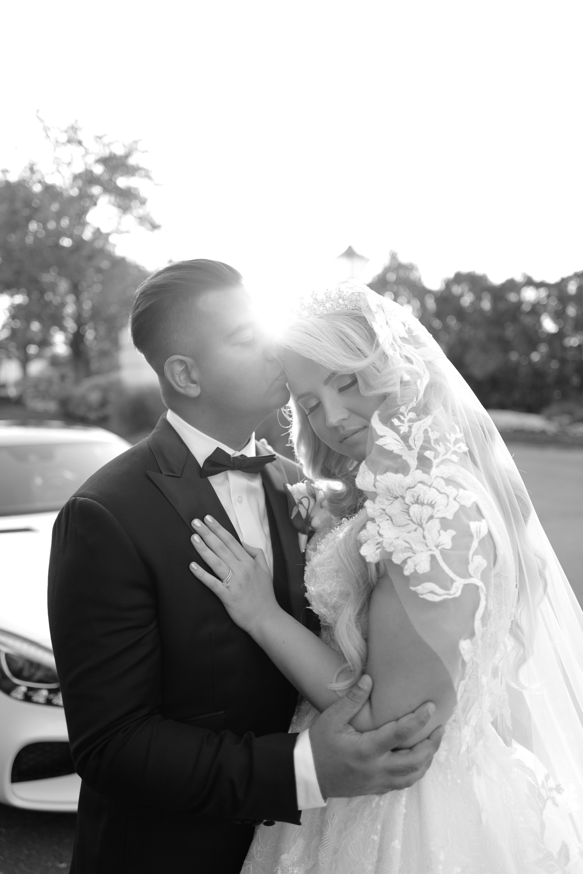 a bride and groom pose for a photo in front of their car