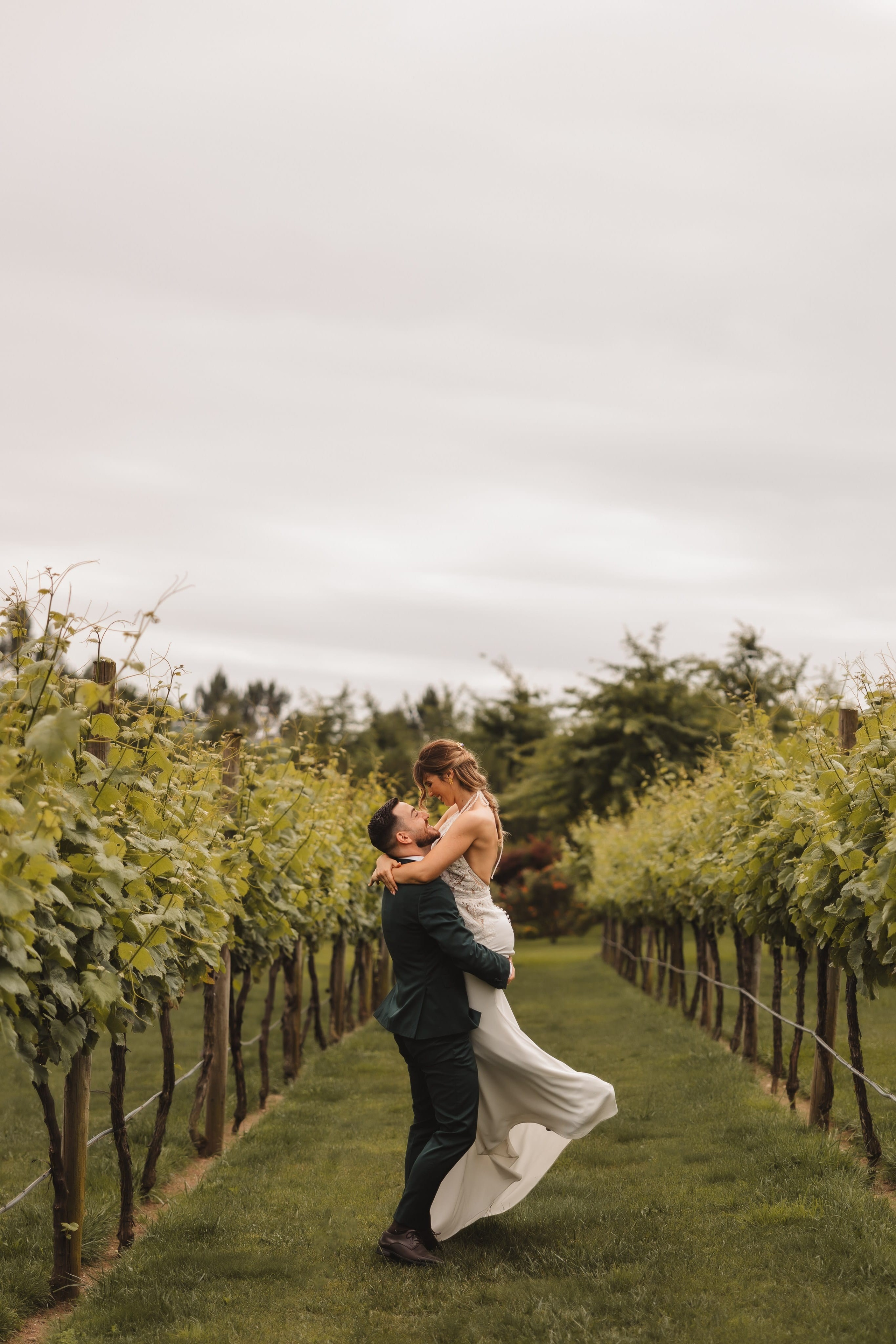 Noiva ao colo do noivo entre vinhas, momento romântico e descontraído de casamento de destino