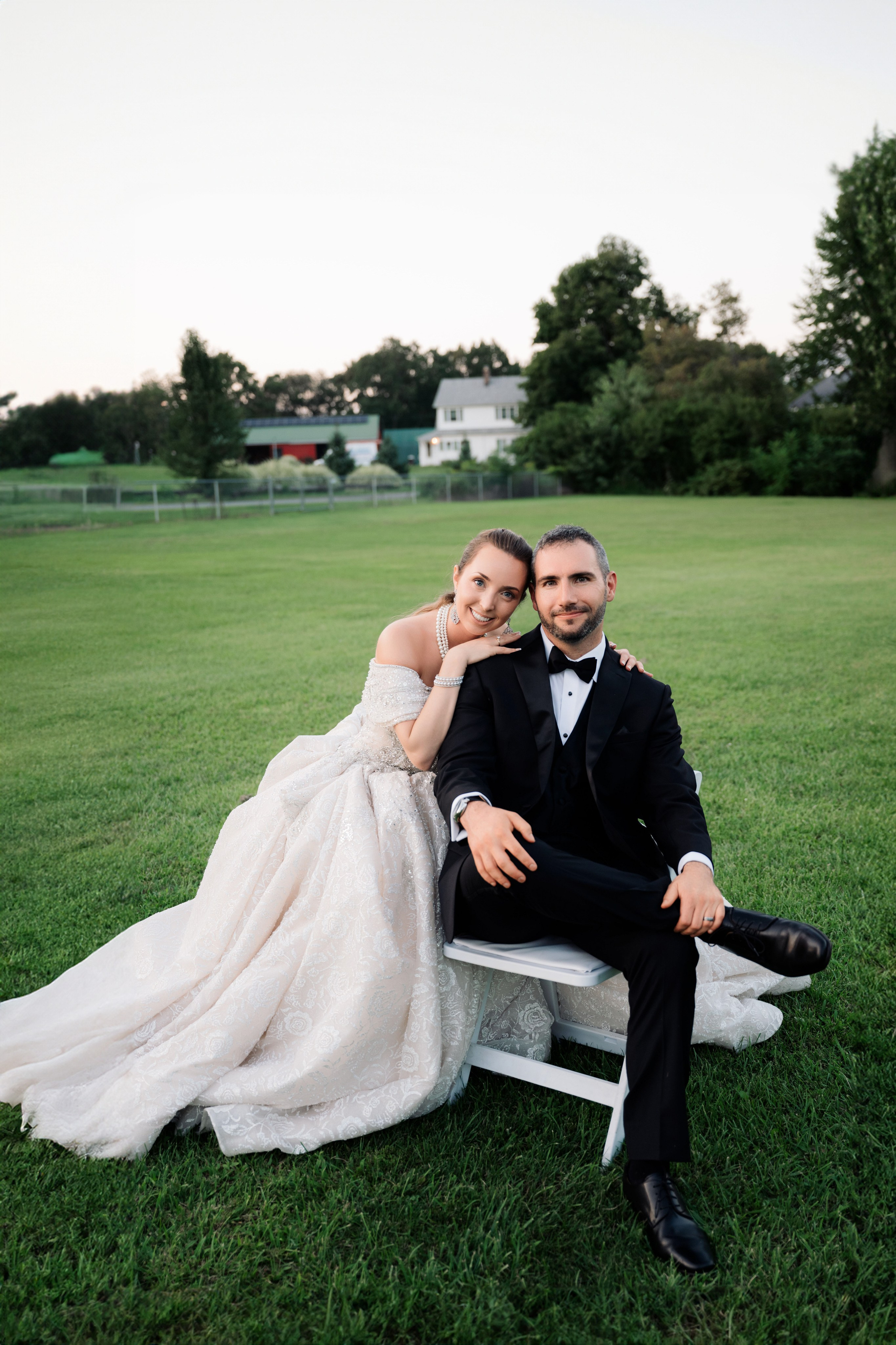 a bride and groom sitting on a bench in a field