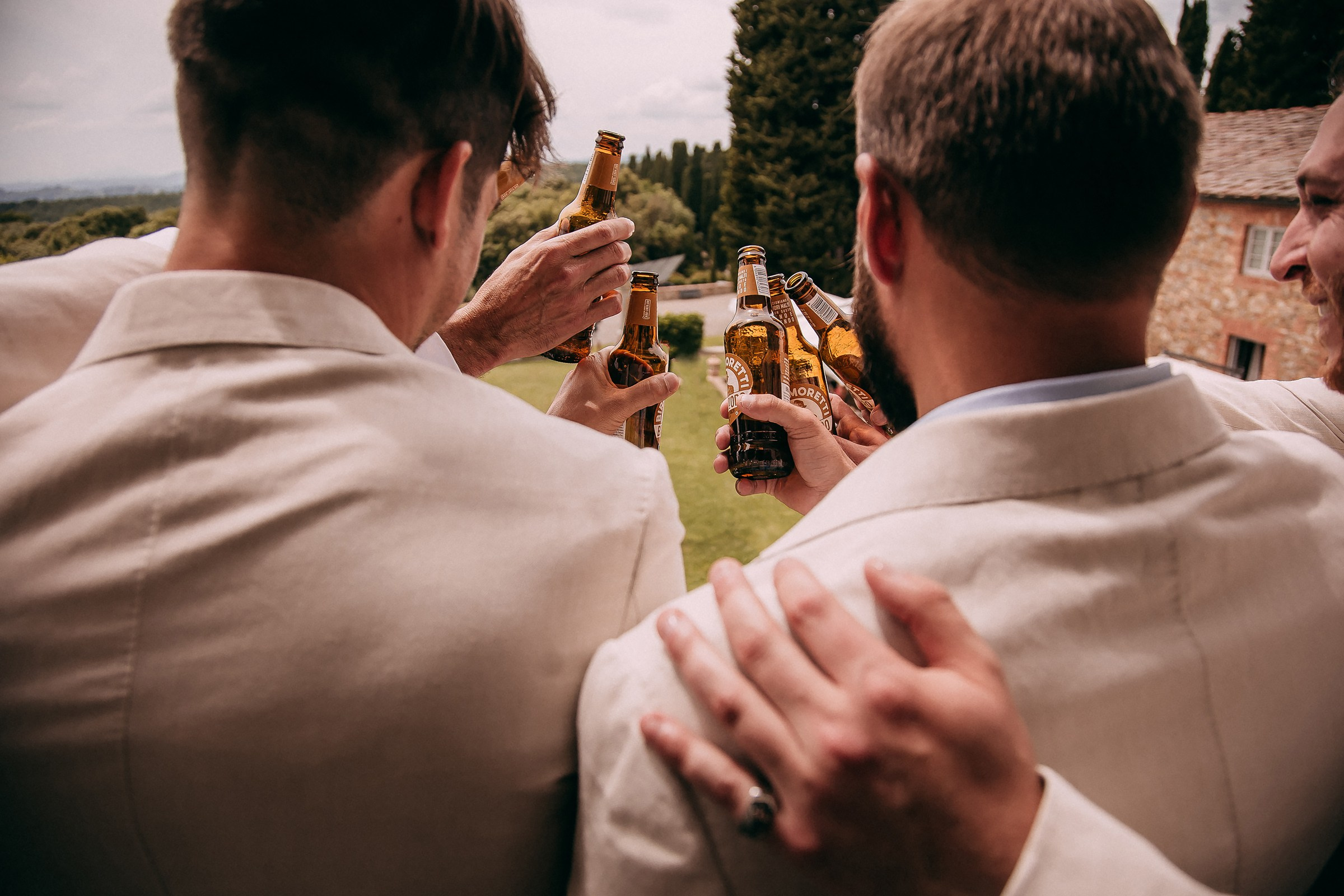 A celebratory toast among friends with bottles raised high, set against a lush Tuscan backdrop.