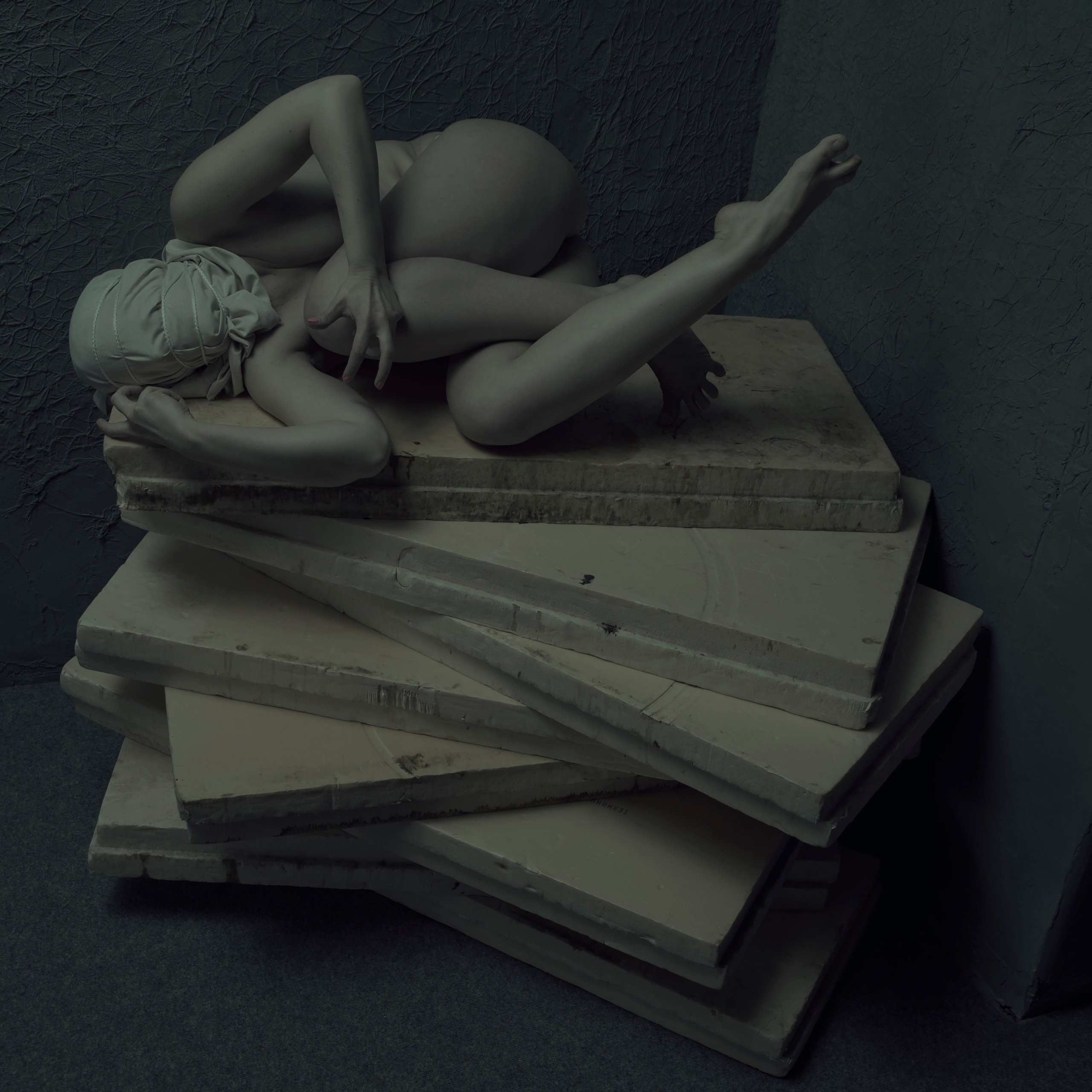 Dramatic photograph of a nude female figure with a concealed face, enveloped in deep shadows and rich tones, featured in Leni Smoragdova's 'Figures Collection: Dark Version' (2019).