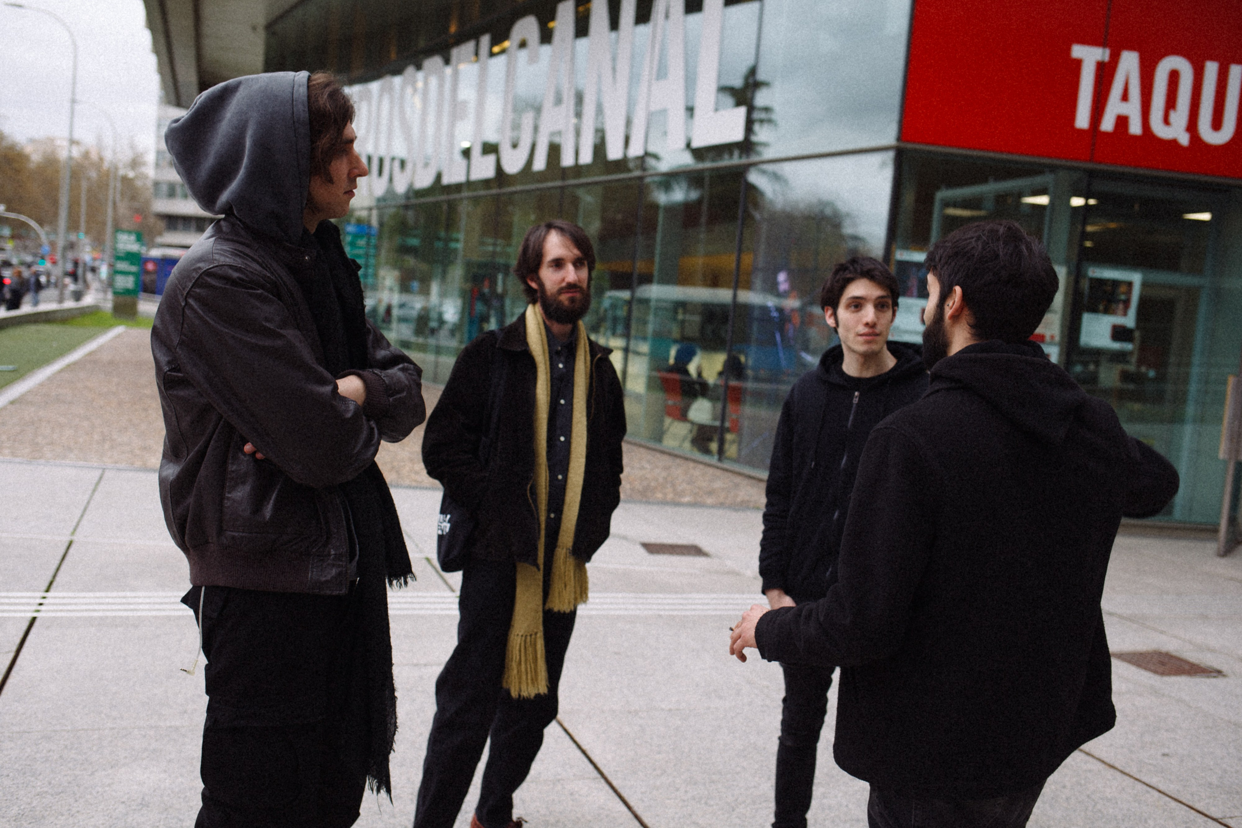 Grupo de hombres vestidos de oscuro conversando fuera de una sala de conciertos