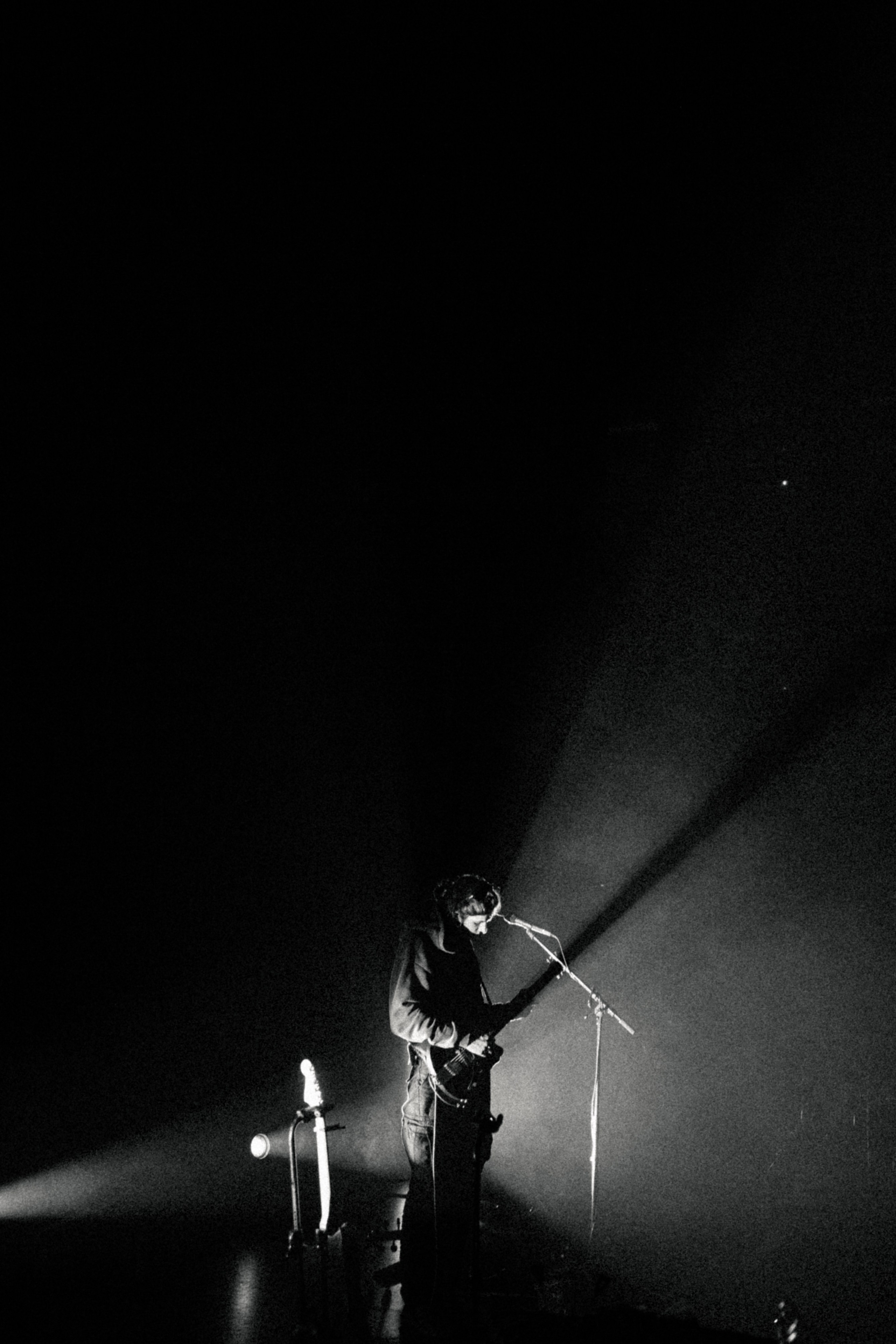 Músico cantando en un micrófono bajo un único foco, en blanco y negro