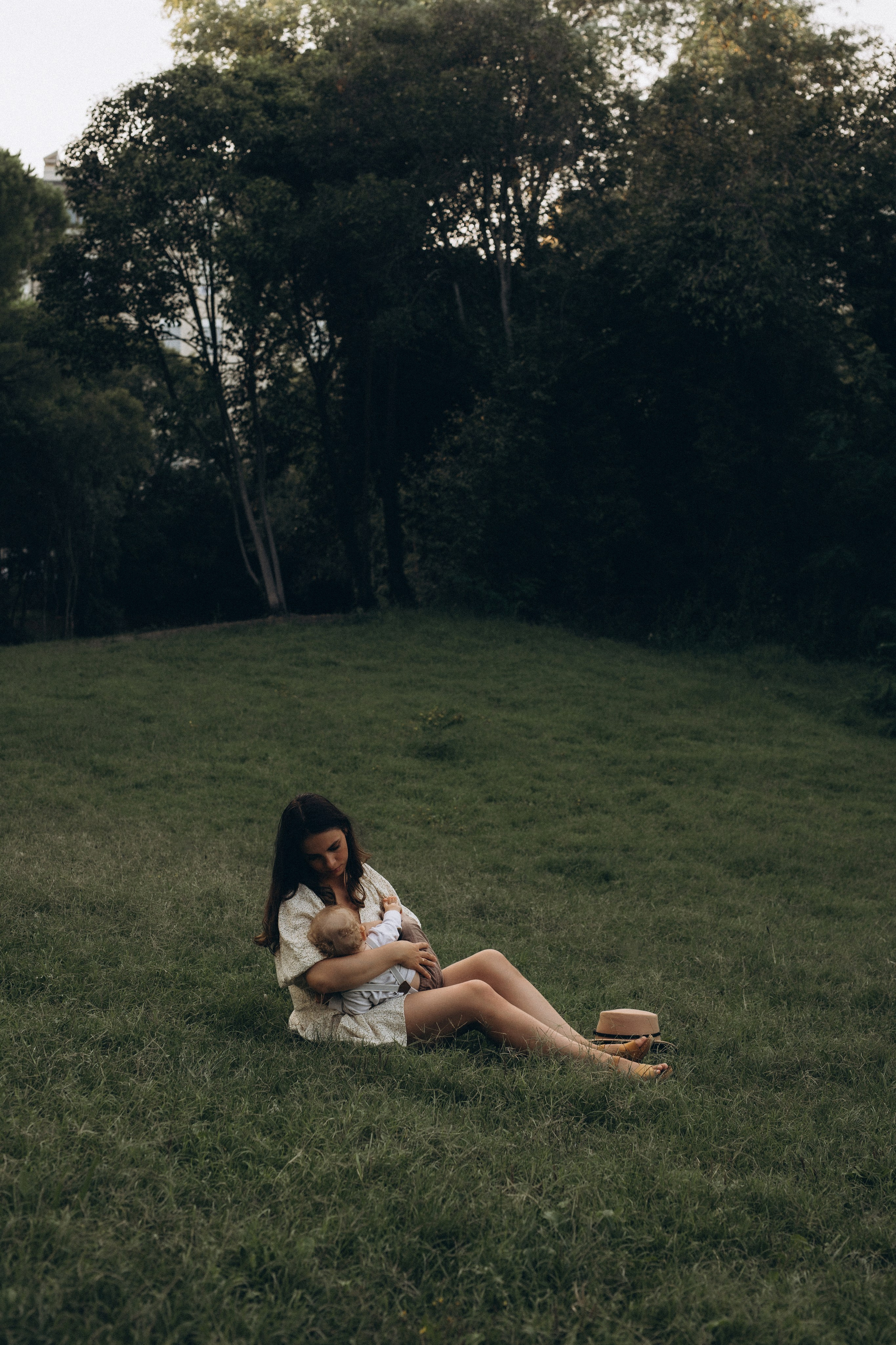 Fotografia di famiglia nella natura a Verucchio: madre seduta sull’erba che tiene in braccio il suo bambino, luce naturale morbida, atmosfera intima e silenziosa, paesaggio verde delle colline dell’Emilia-Romagna, servizio fotografico familiare all’aperto.