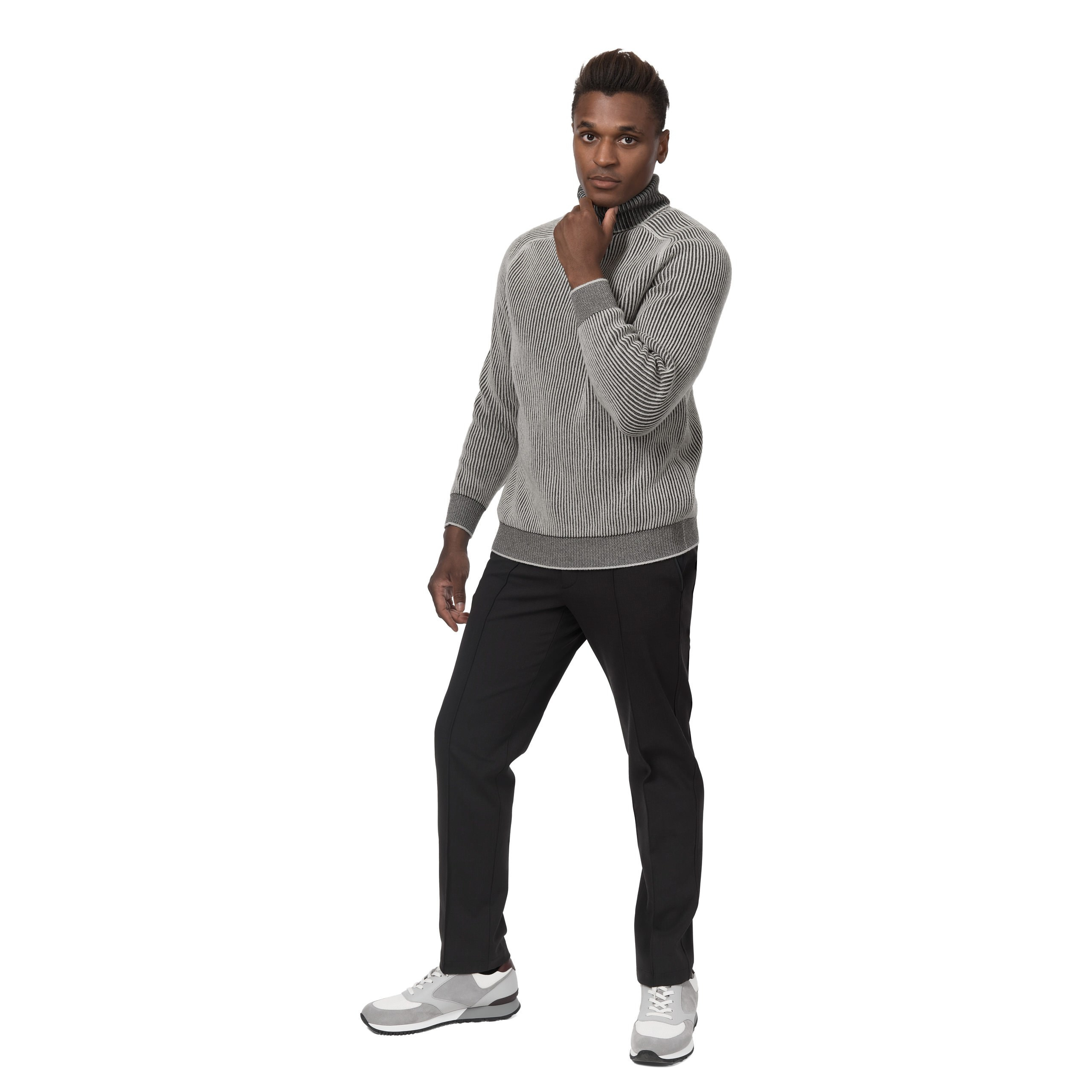 Model in grauem Pullover und schwarzer Hose, Ganzkörperaufnahme im Studio.