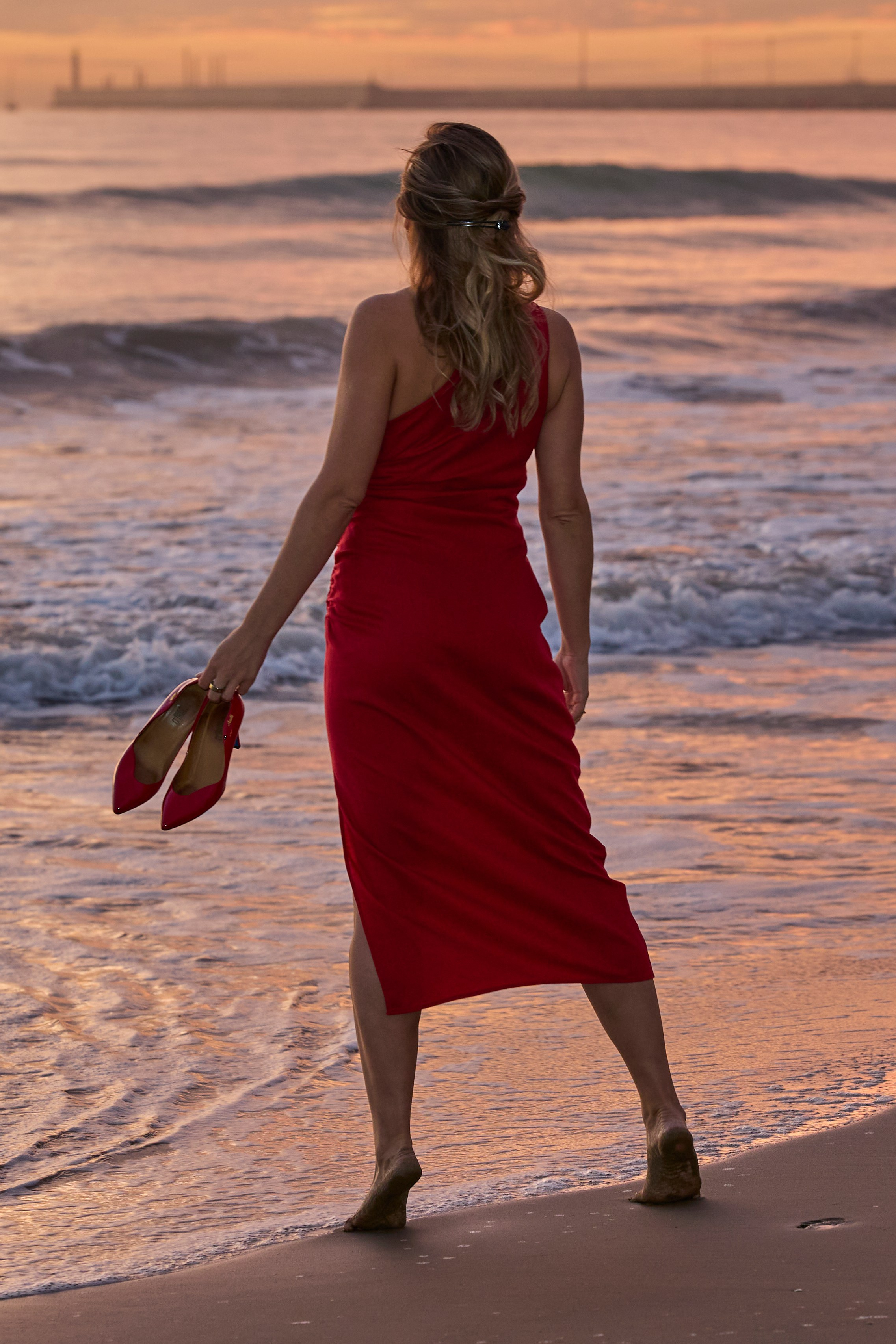 Mujer con vestido rojo caminando por la playa de La Malvarrosa al amanecer en Valencia