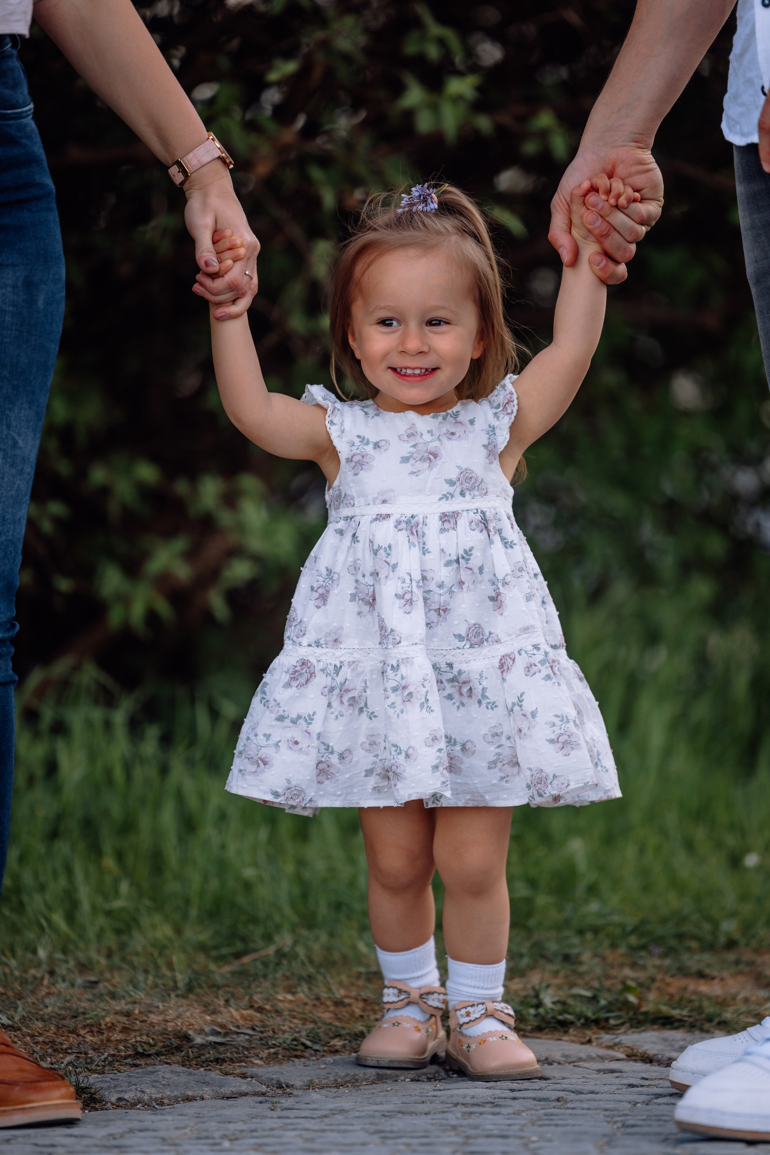 Kleine Tochter hält die Hände ihrer Eltern beim Spaziergang durch den Schlosspark