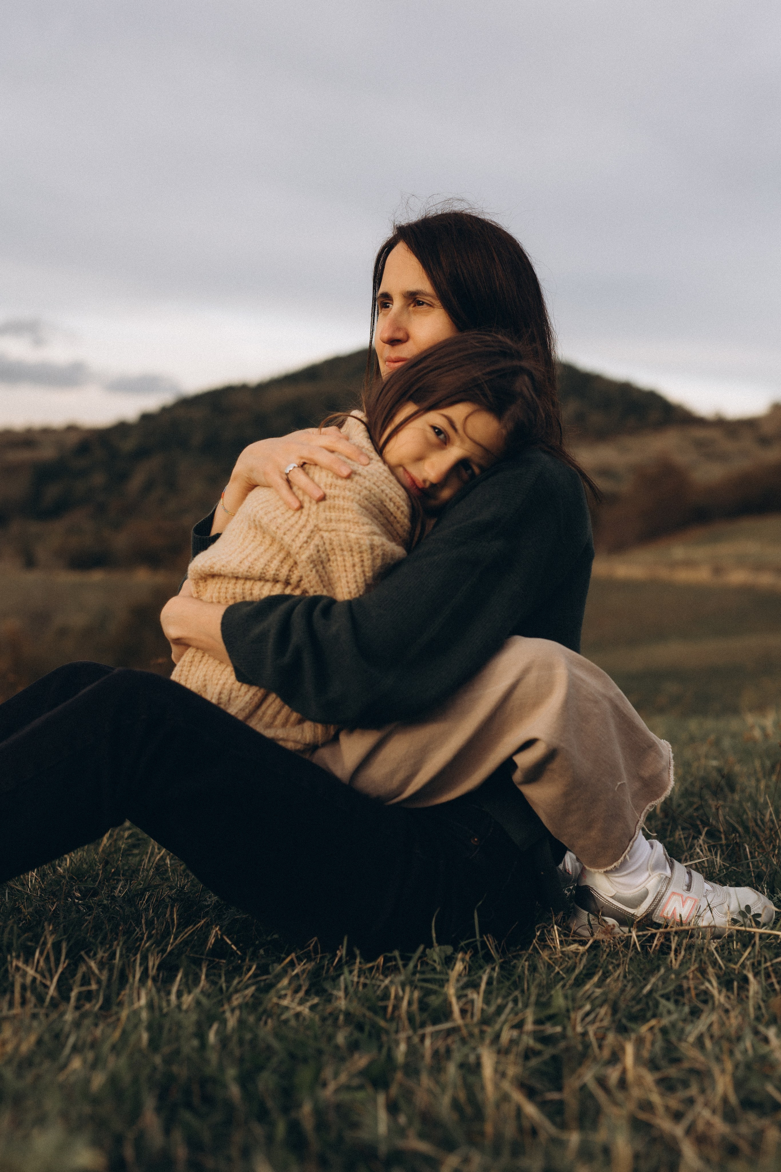 Madre che abbraccia la figlia seduta sull’erba a Villa Verucchio, un momento di calma, contatto fisico e intimità familiare nella natura.