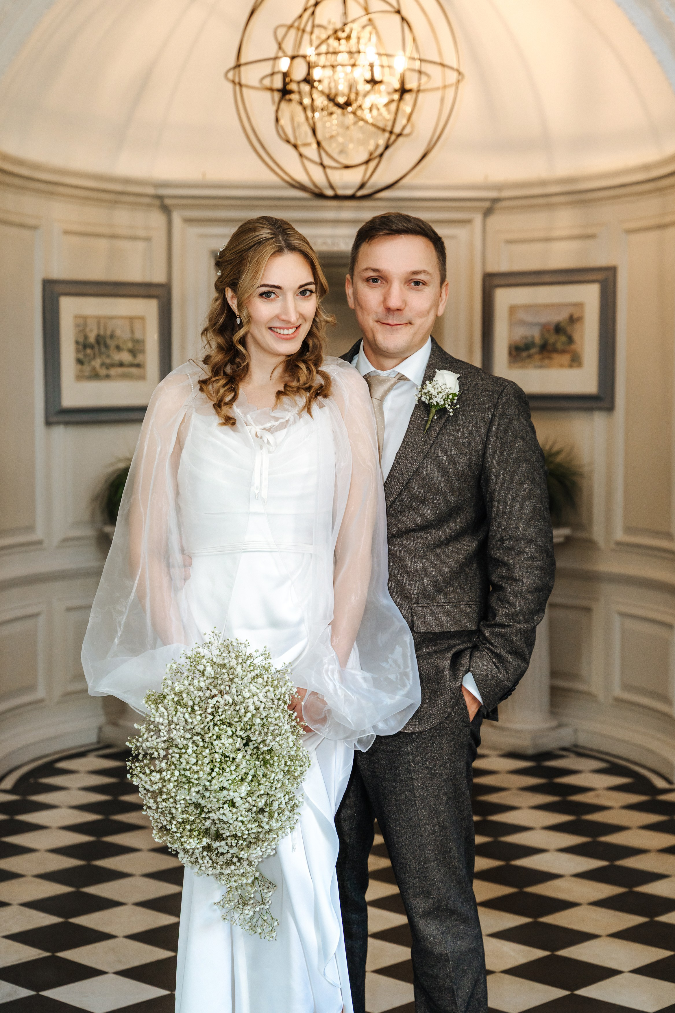 Andrey and Elena pose together in the elegant interior of Barnet Hill Hotel, featuring a grand staircase and classic architectural details.