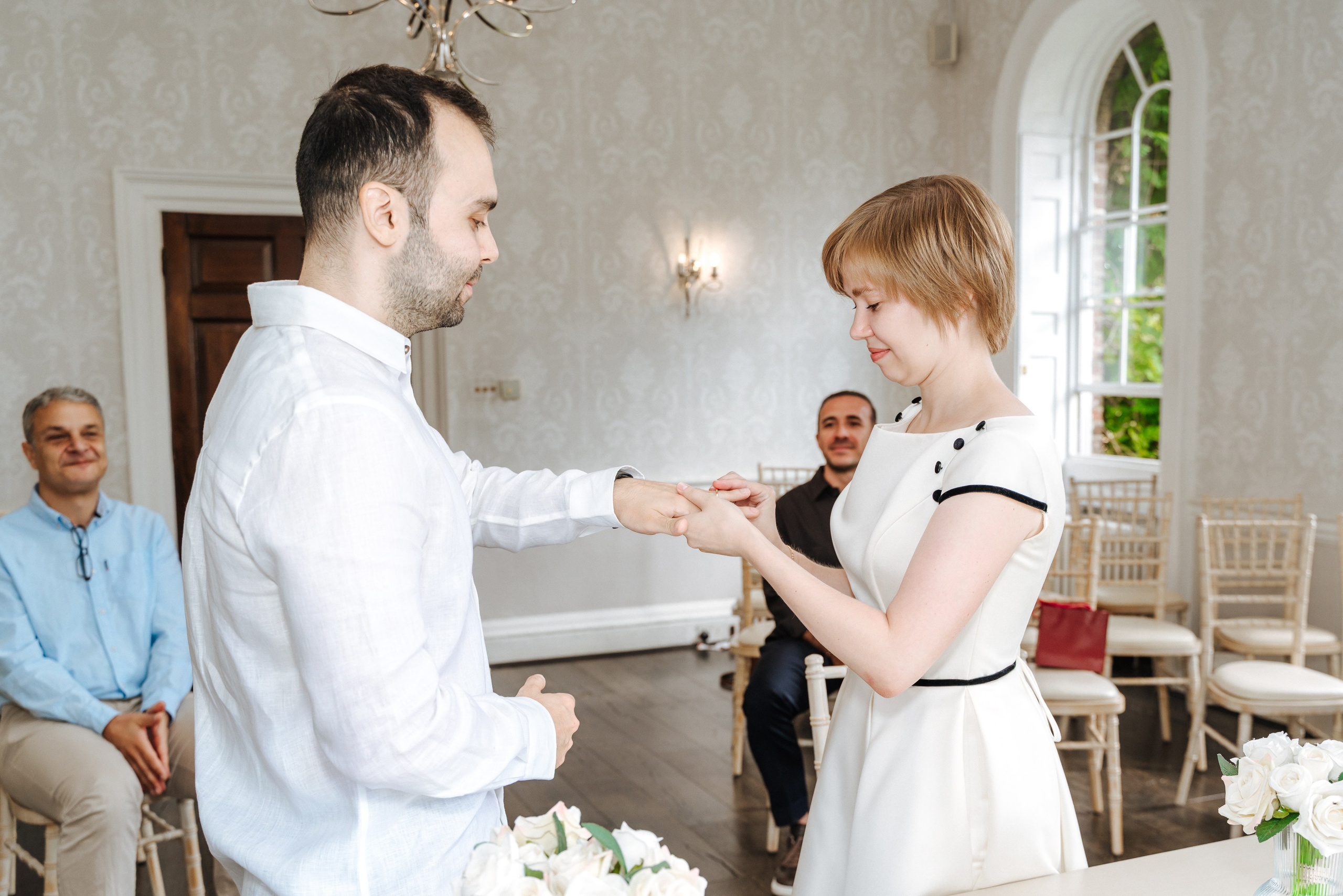 The bride slips the wedding ring onto his groom’s finger at Merton Register Office