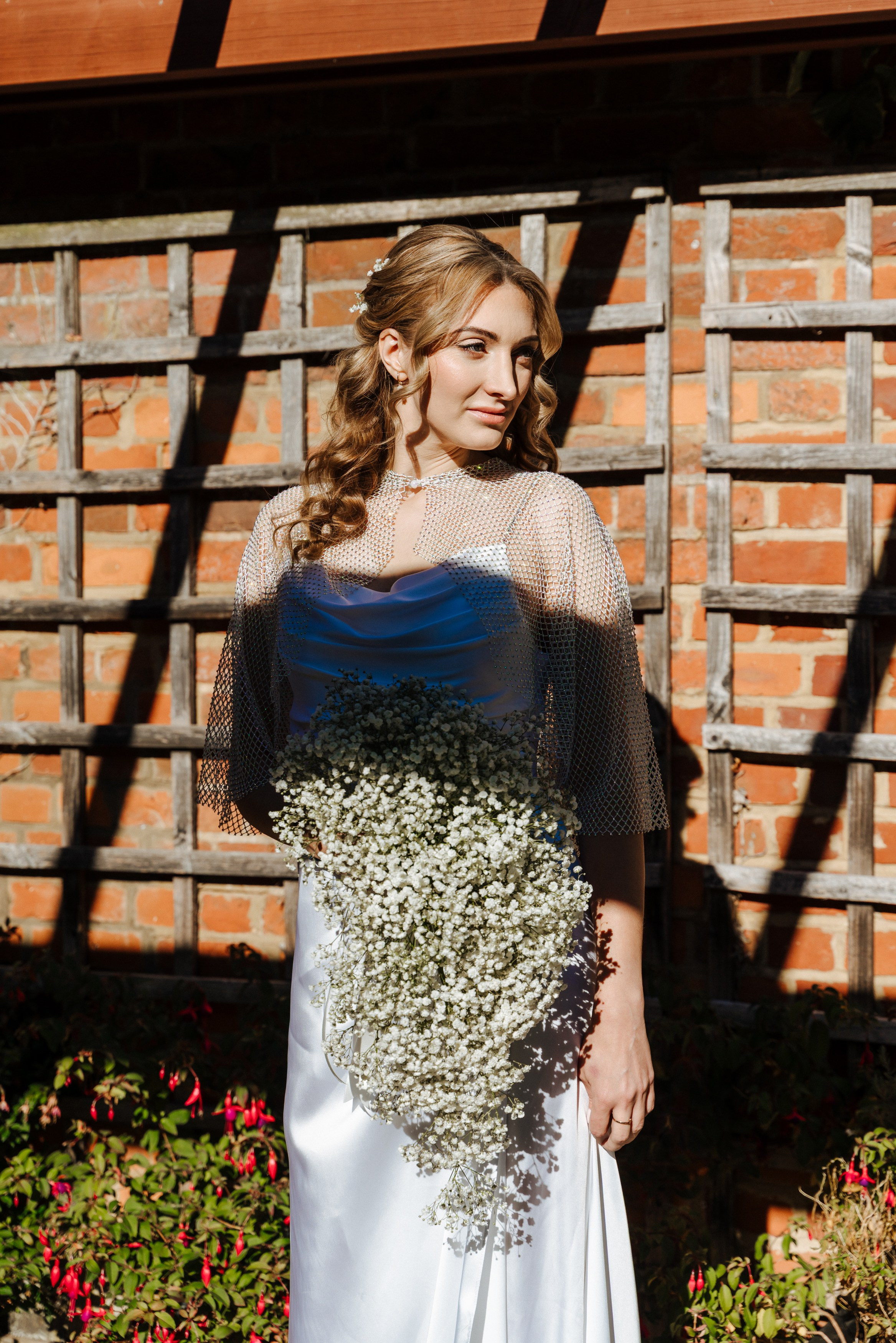 Bride Elena in an elegant white satin wedding dress holding a delicate gypsophila bouquet, photographed in natural light.