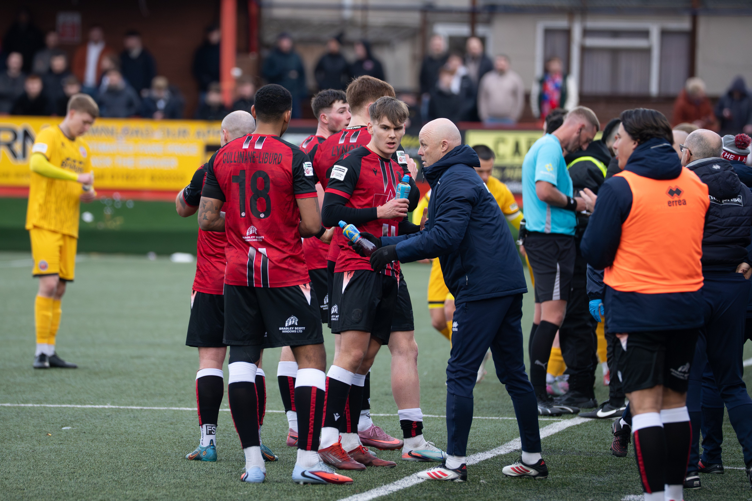 Tamworth, England — February 14, 2026: Tamworth’s Jordan Cullinane-Liburd and Oliver Lynch take on refreshments from a member of the coaching staff during a stoppage in play at The Lamb Ground ahead of the Enterprise National League match between Tamworth and Aldershot Town. Photo: Jay Soundo