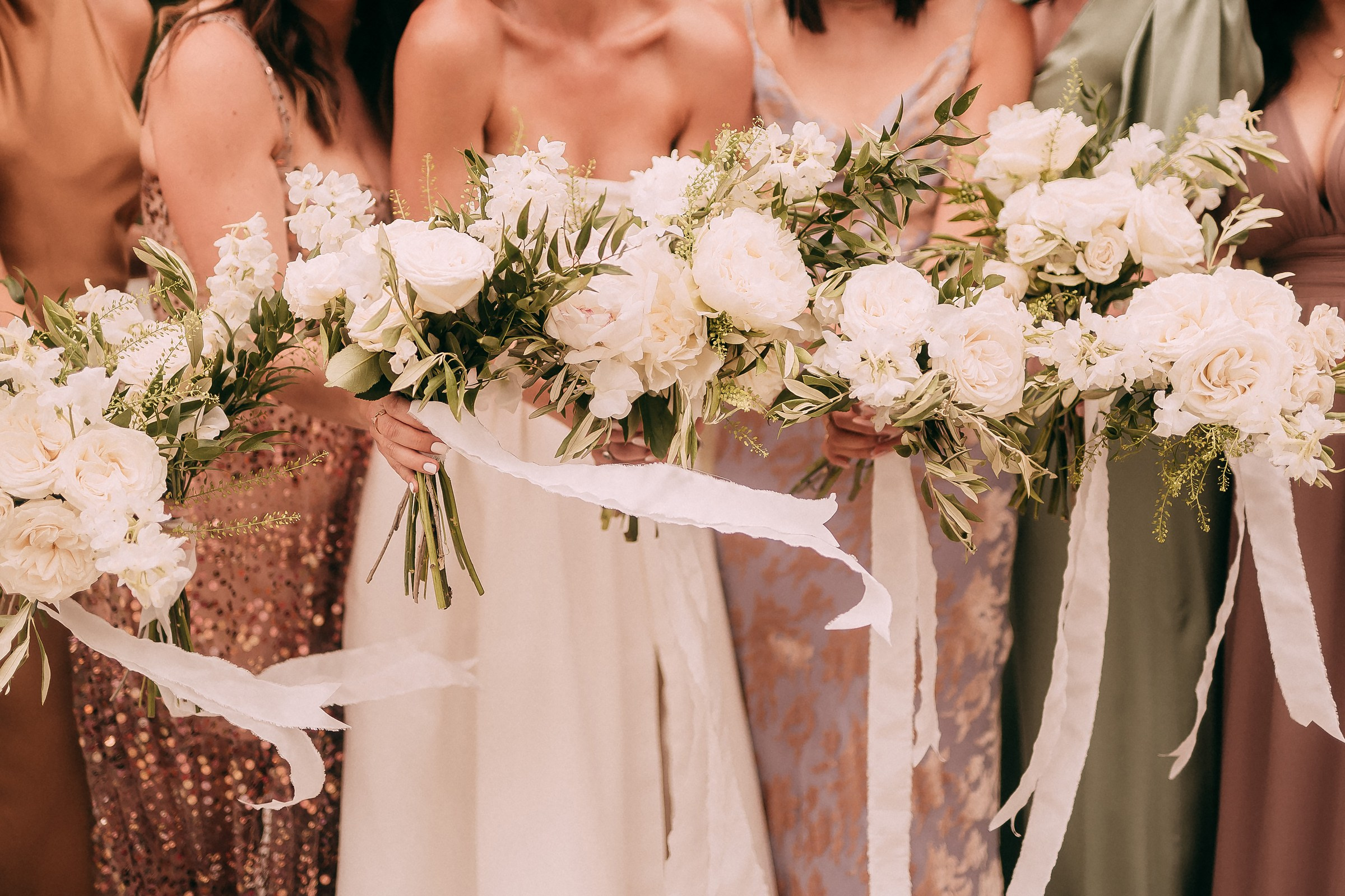 Close-up of bridesmaids’ bouquets featuring white roses, greenery, and flowing ribbon accents, perfectly aligned in their hands.