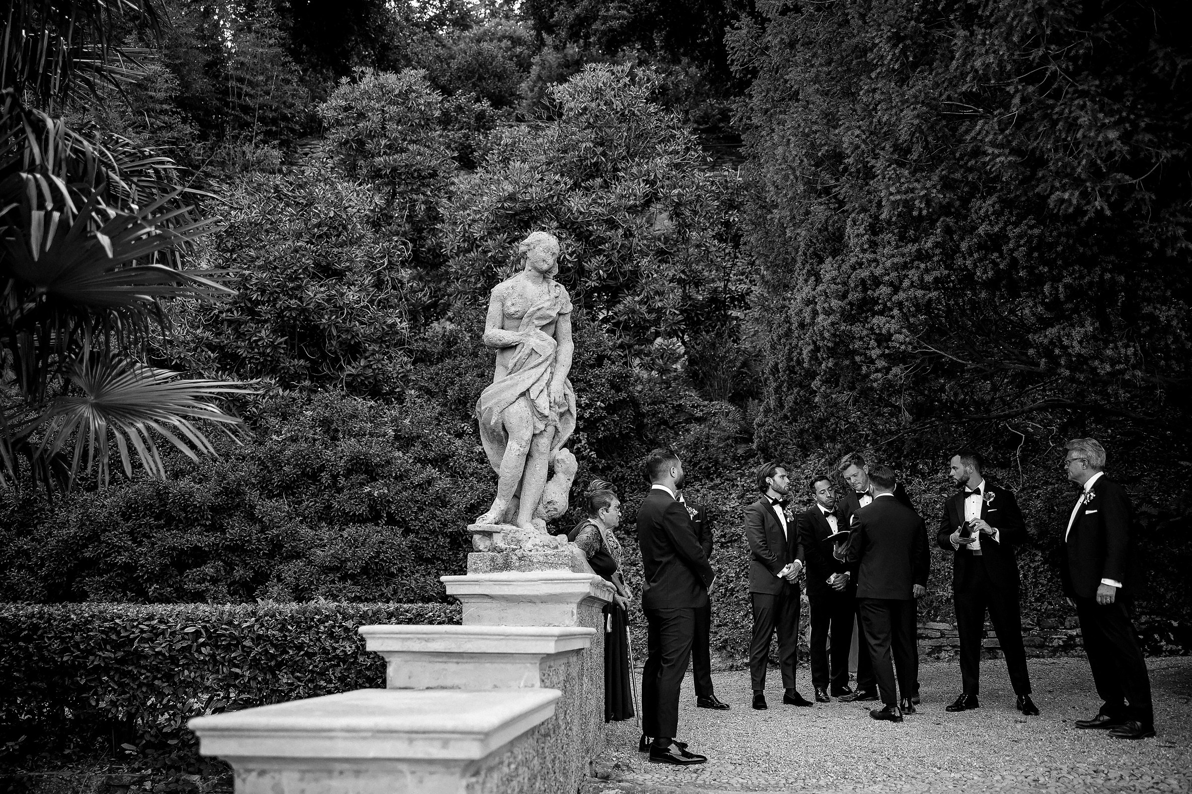 A group of dapper groomsmen elegantly gathered around a stunning garden statue.