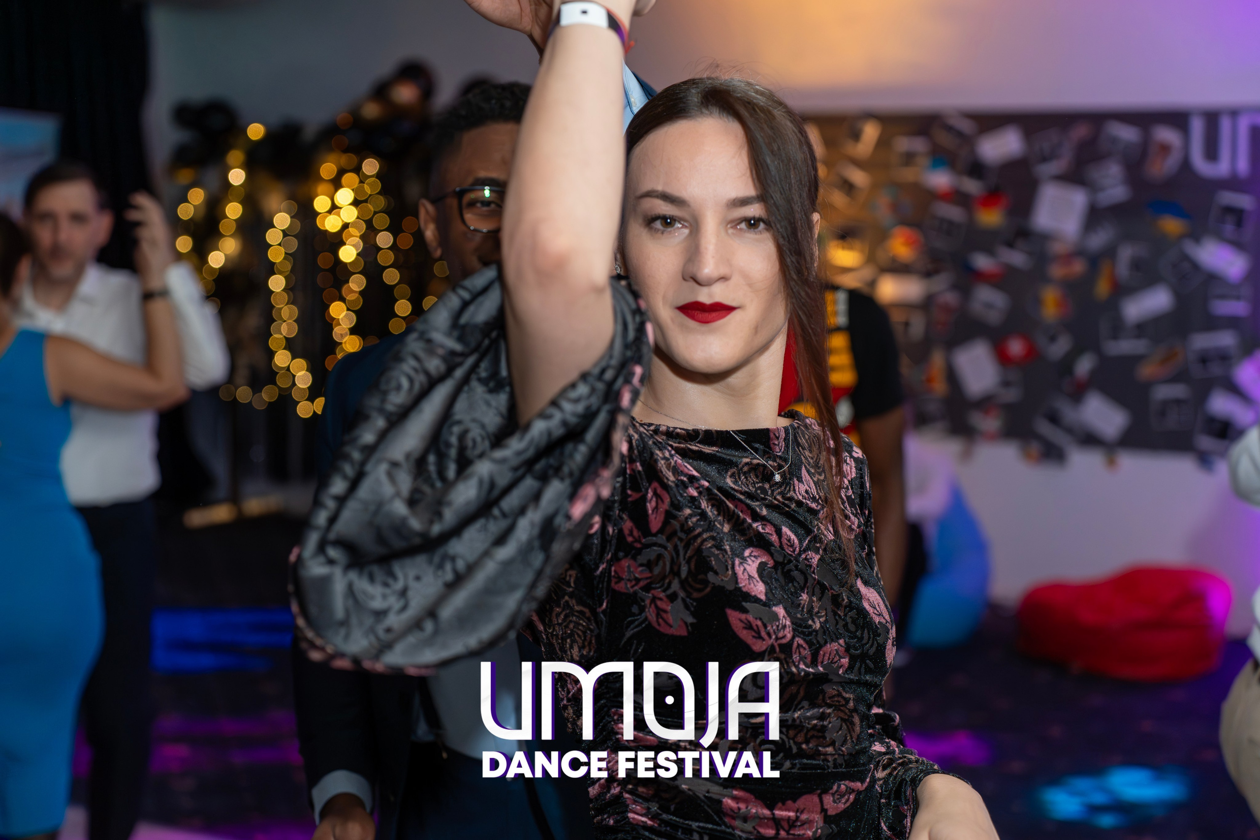 Woman dancing at an indoor event with blurred people and string lights in the background.