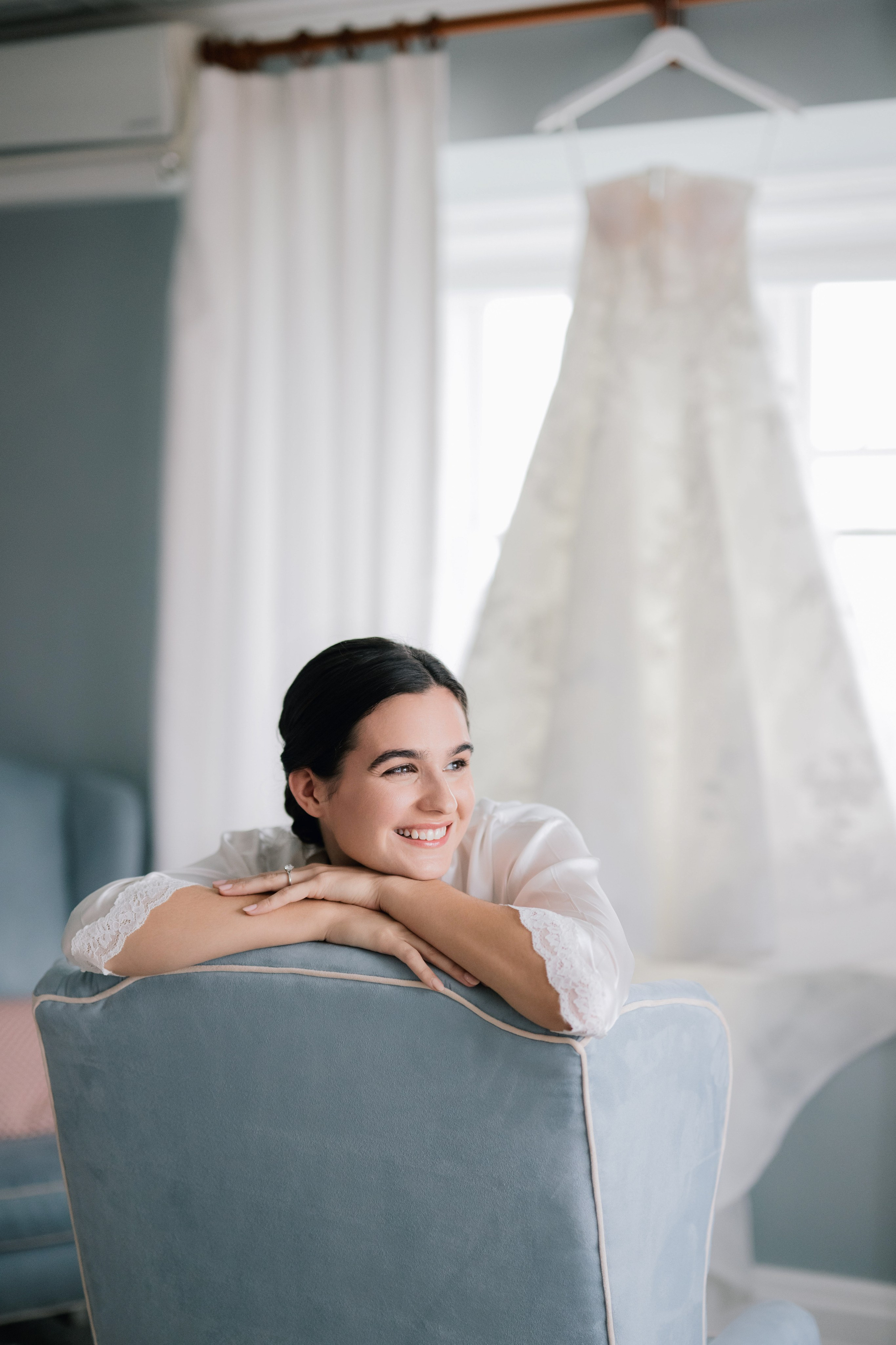a woman sitting in a chair with a wedding dress hanging on the wall