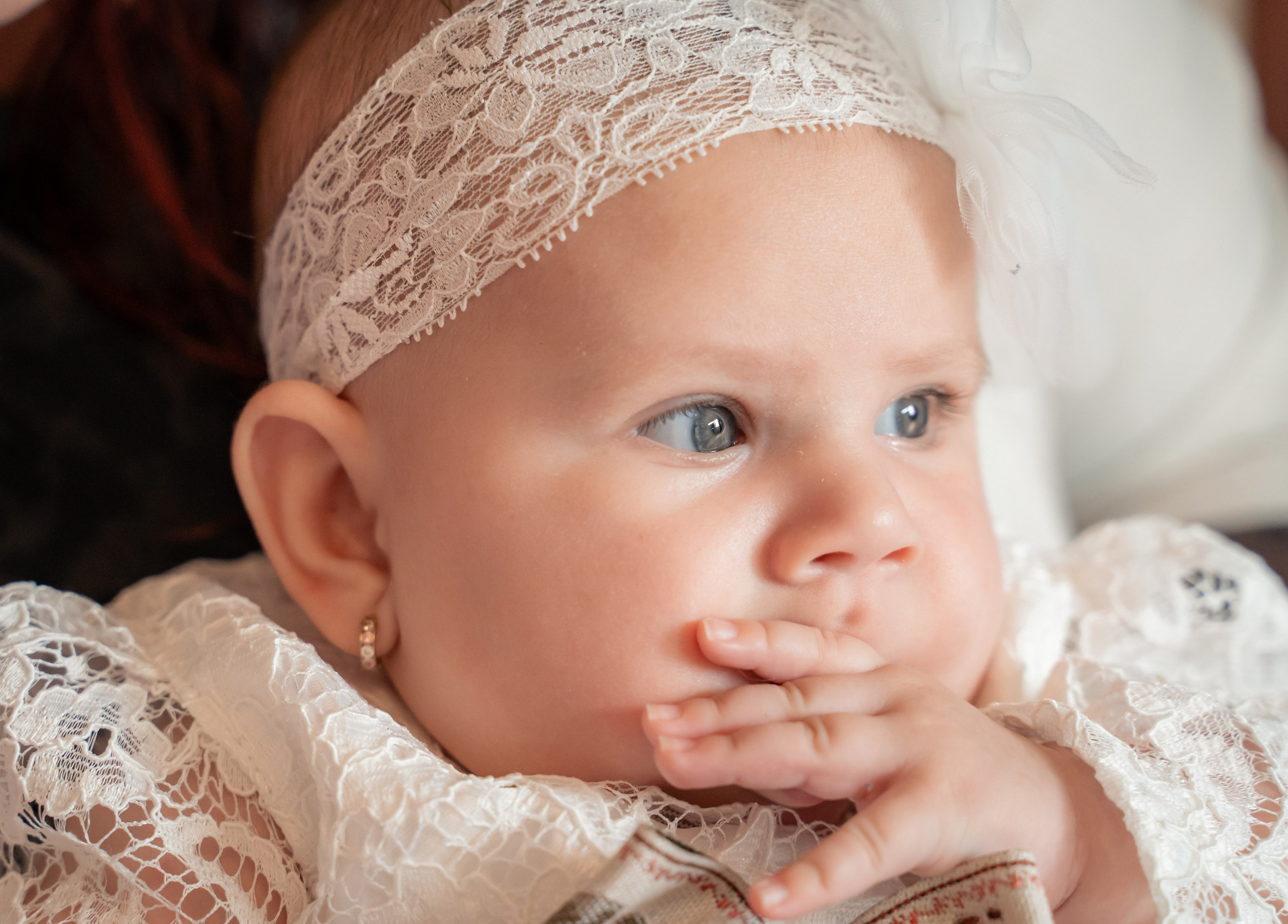 Portret de aproape cu un bebeluș la botez, fetiță purtând bentiță din dantelă albă și rochiță elegantă, fotografie de botez incadru.ro București.
