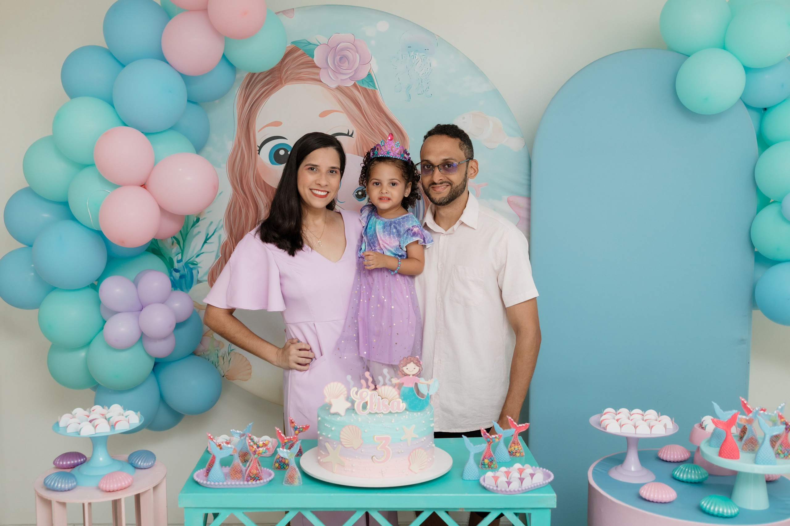 Elisa com os pais na mesa do bolo