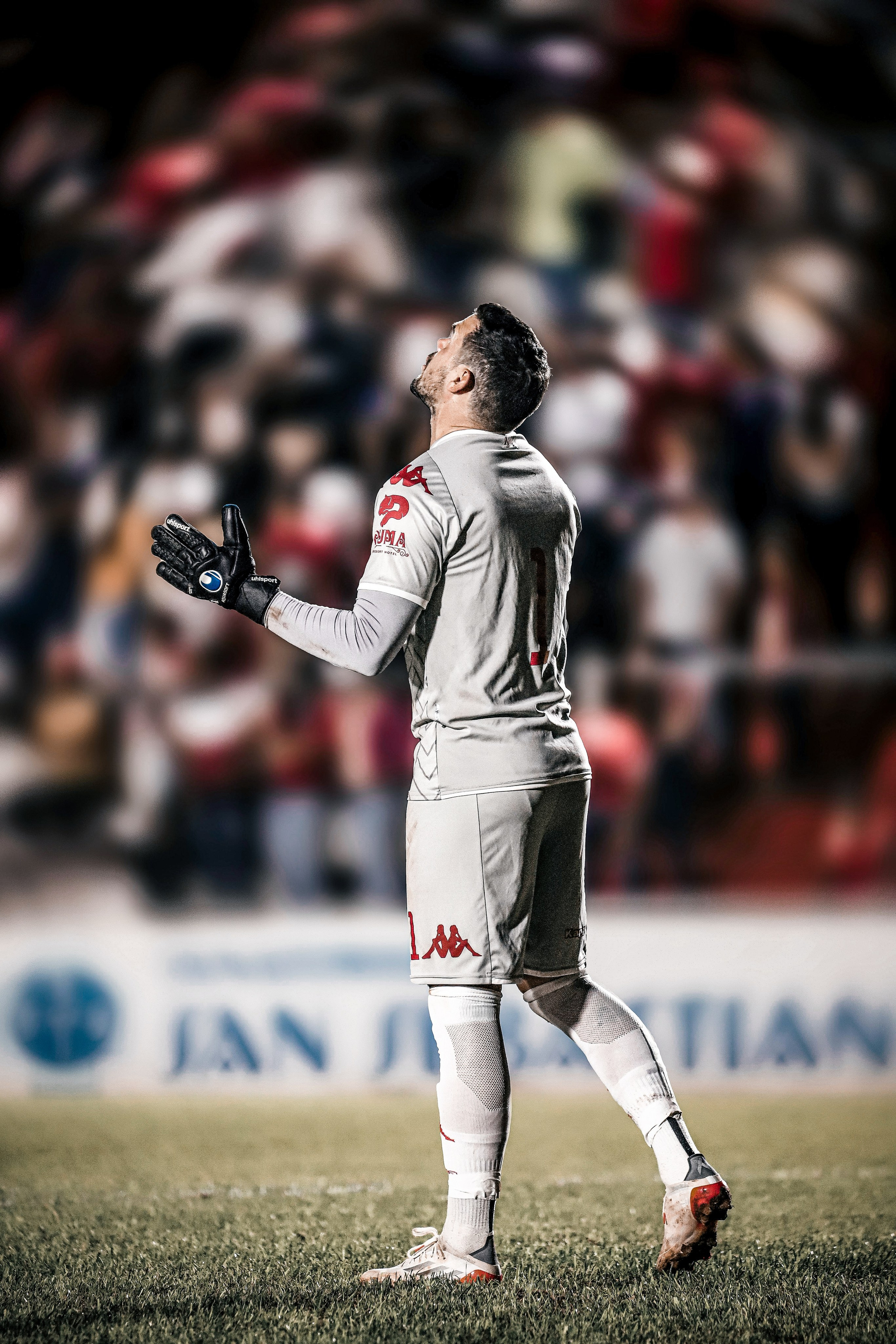 Goalkeeper in white kit during a football match with crowd in background, matchday football photography.
