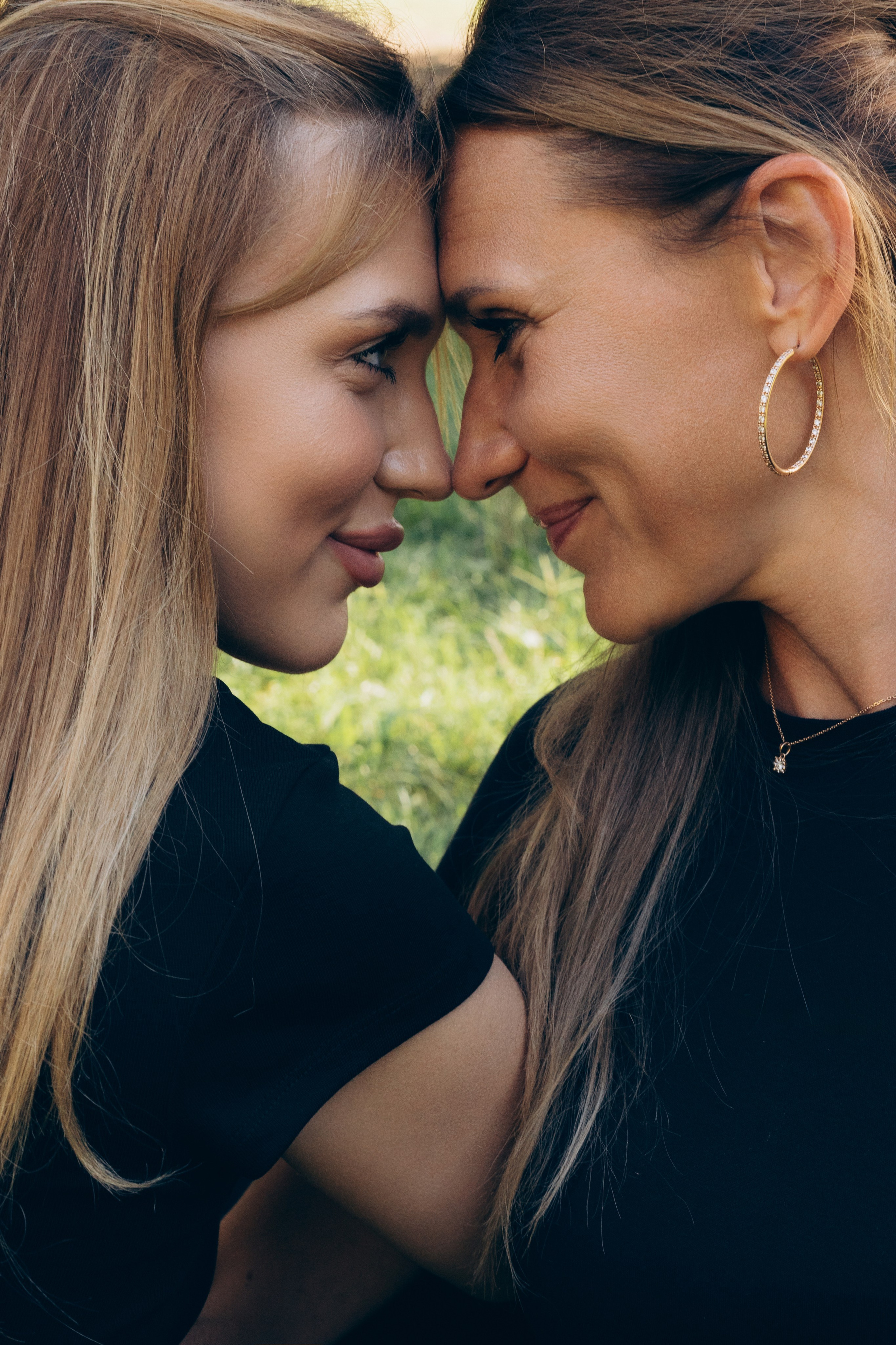 Servizio fotografico di madre e figlia adulta, ritratto ravvicinato di due donne che si guardano negli occhi, connessione emotiva e legame tra generazioni in un contesto naturale.