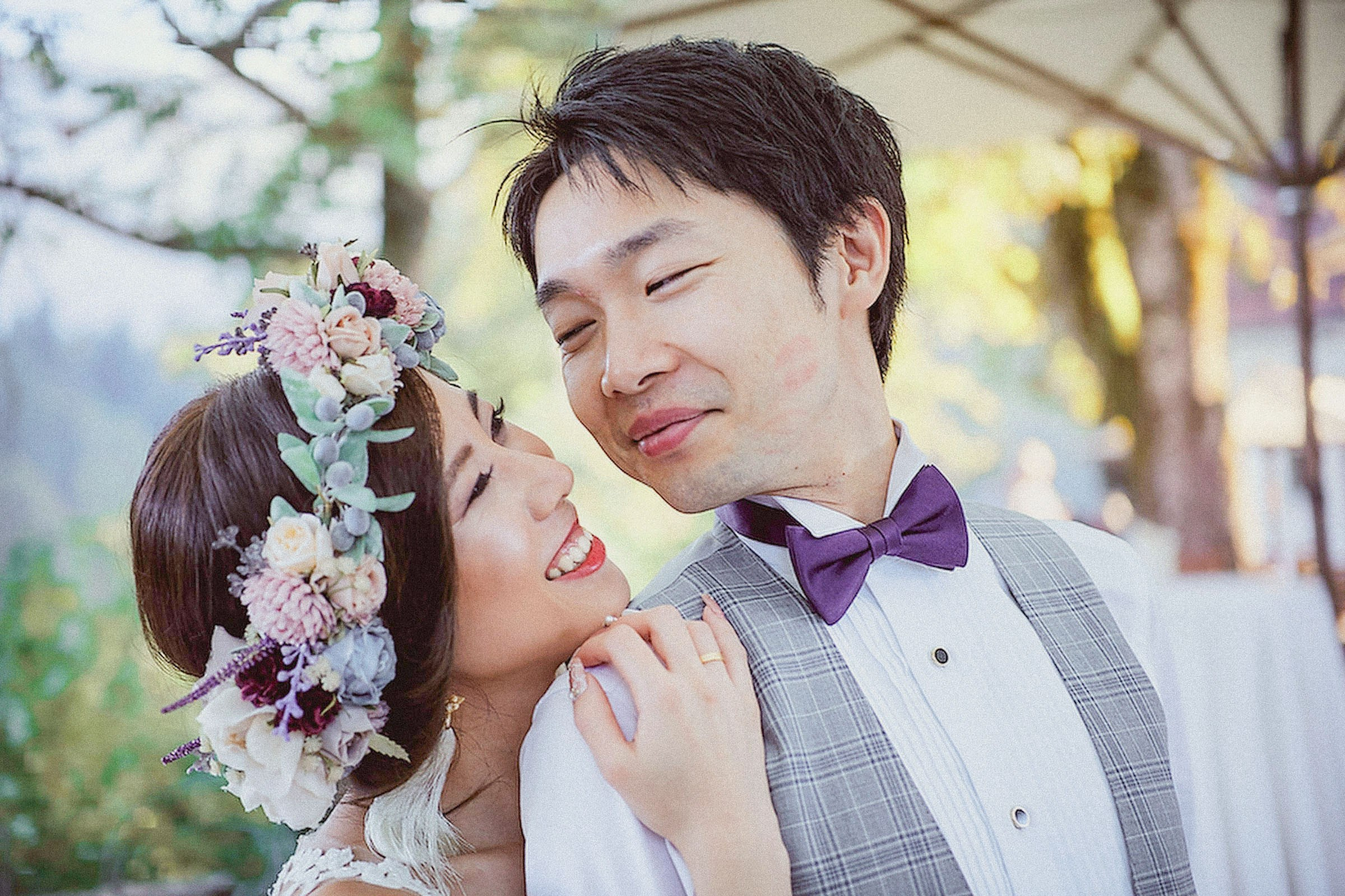 A Japanese bride, wearing a floral headpiece stands behind her groom as she looks lovingly into his eyes.
