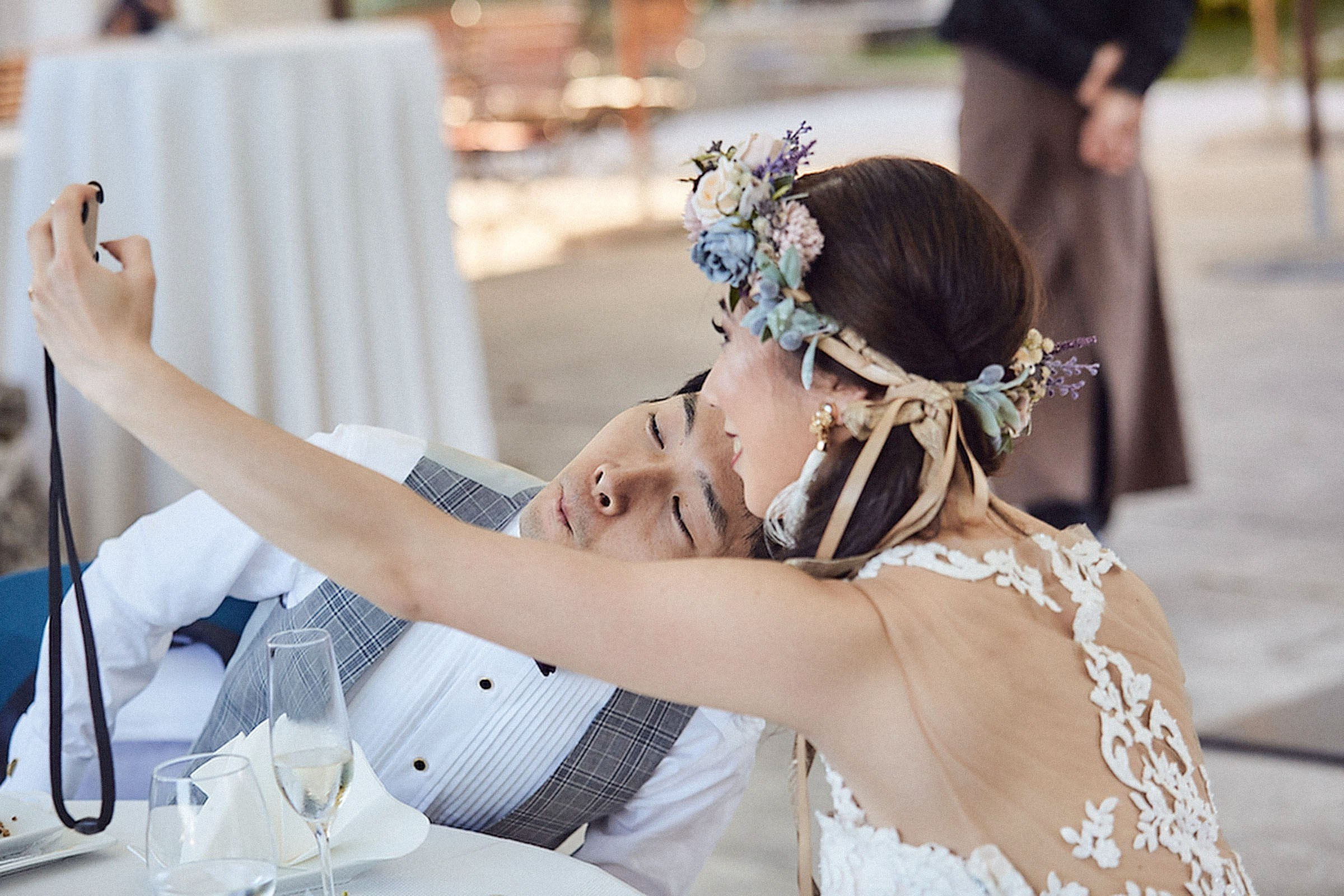 A bride wearing a floral headpiece takes a selfie picture of herself and her groom.