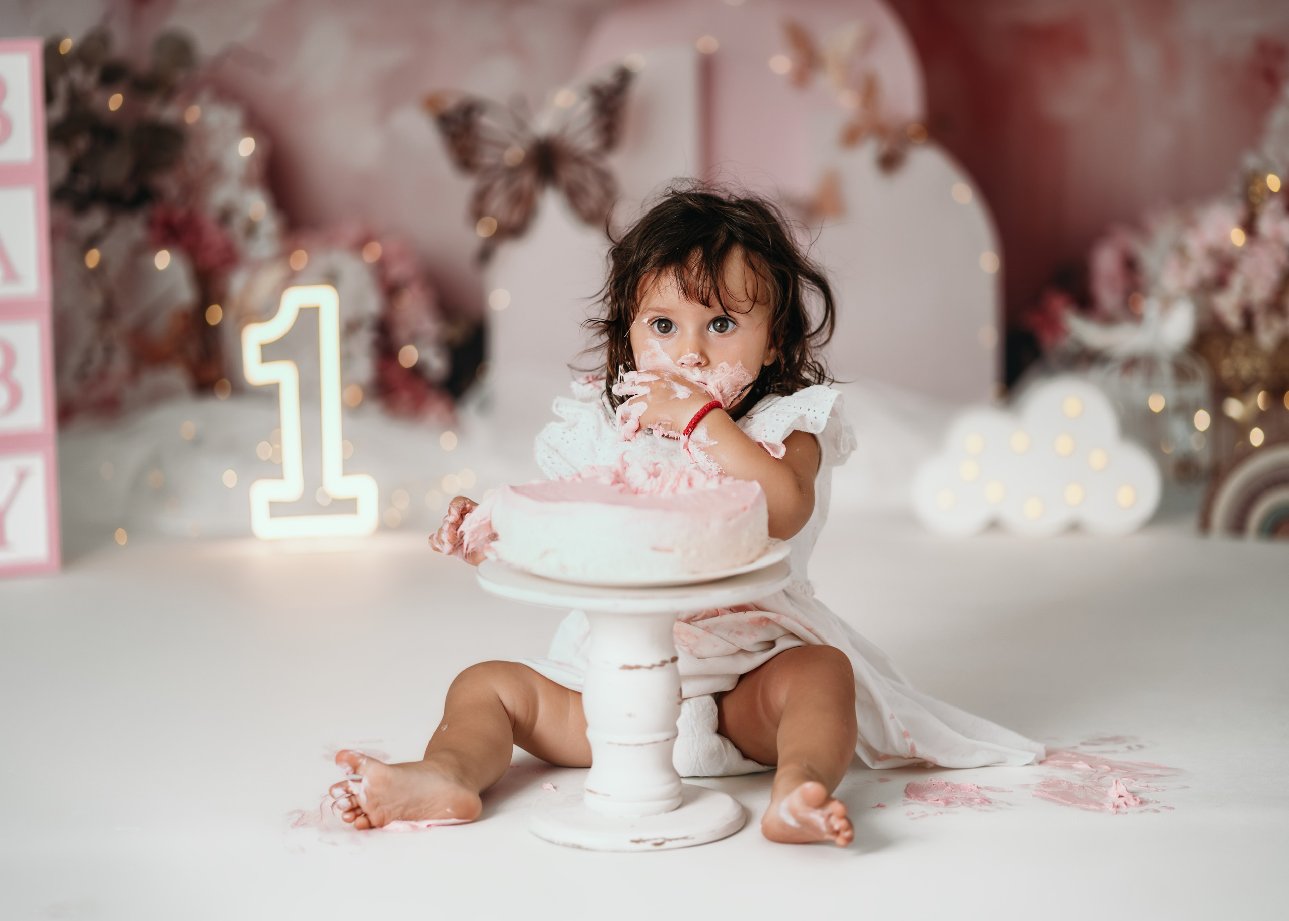 Prvi rođendan slikanje – beba u beloj haljinici u roze scenografiji sa balonima