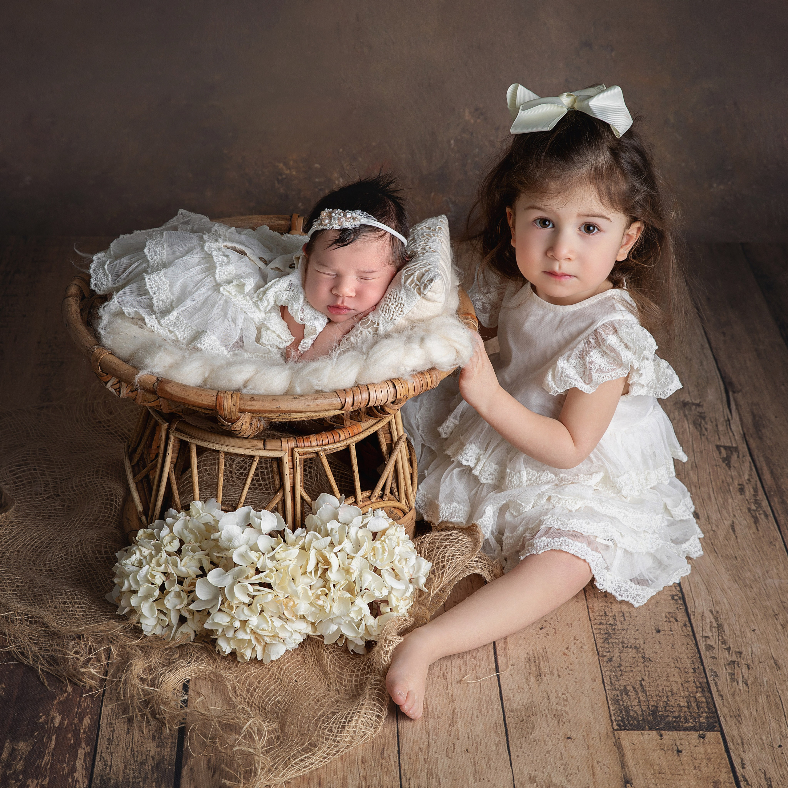"Ett äldre syskon som sitter försiktigt bredvid sin nyfödda bror eller syster. Denna bild fångar den ömma och beskyddande relationen mellan syskonen och är idealisk för nyfödda fotograferingar."