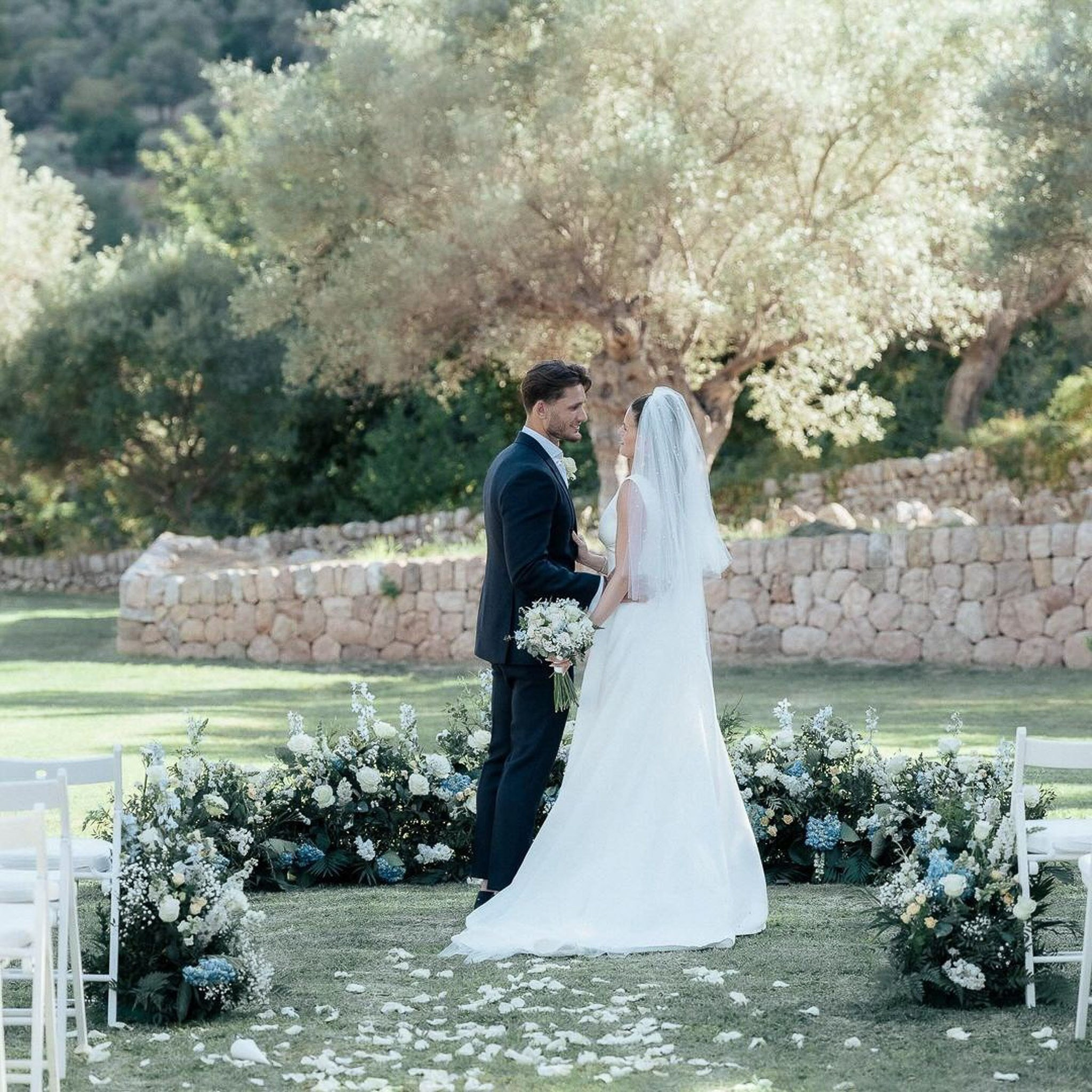 Bride and groom facing each other among white and blue floral aisle decor at their outdoor Mallorca wedding