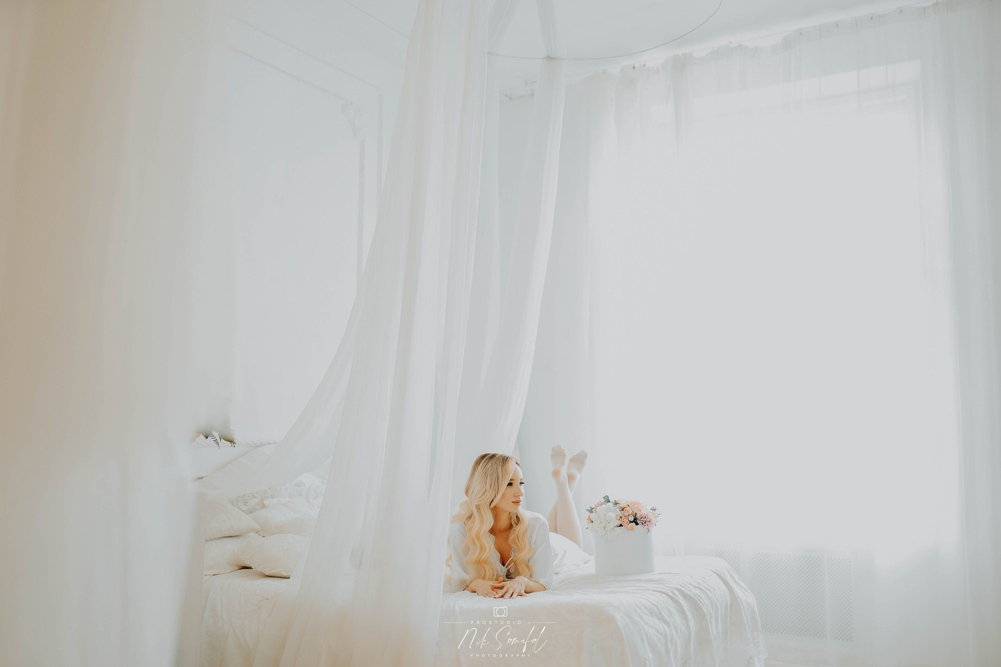 Bridal boudoir morning photography Miami — bride in a white canopy bed with flowers