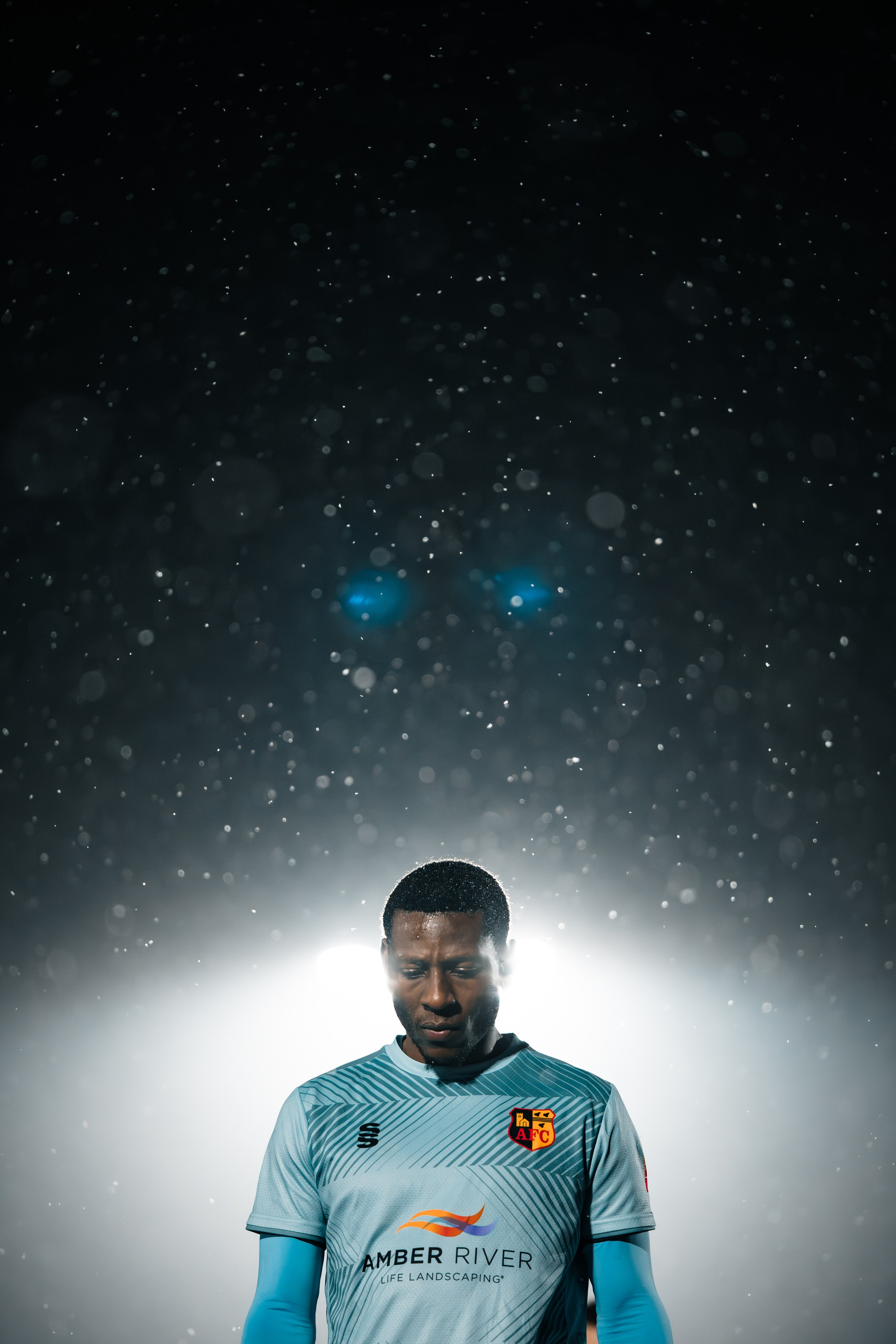 Editorial-style football portrait of a player in a light blue kit under dramatic lighting, athlete portrait photography.