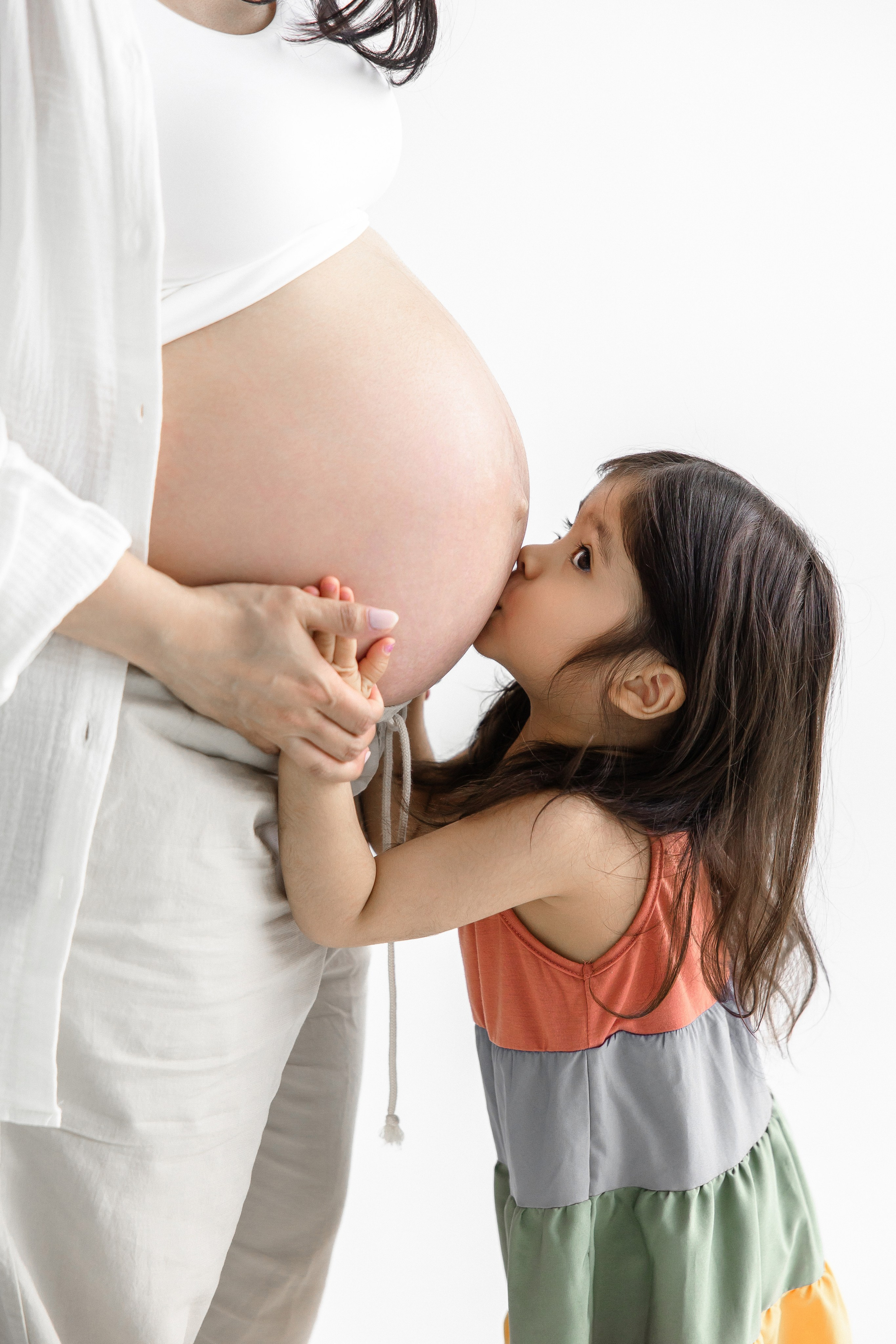 Little girl kissing her pregnant mom’s belly during maternity photoshoot – emotional family-centered pregnancy photography in Toronto by Iana Banana