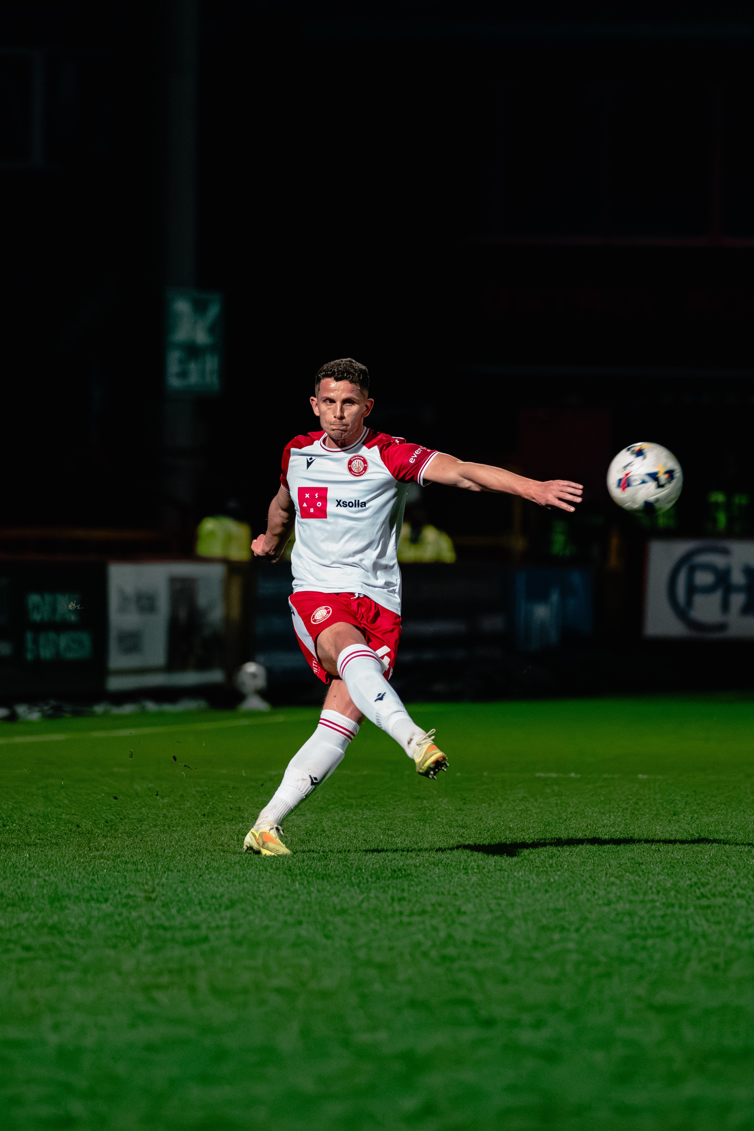 Stevenage player striking the ball during the League One fixture against Leyton Orient under the floodlights.