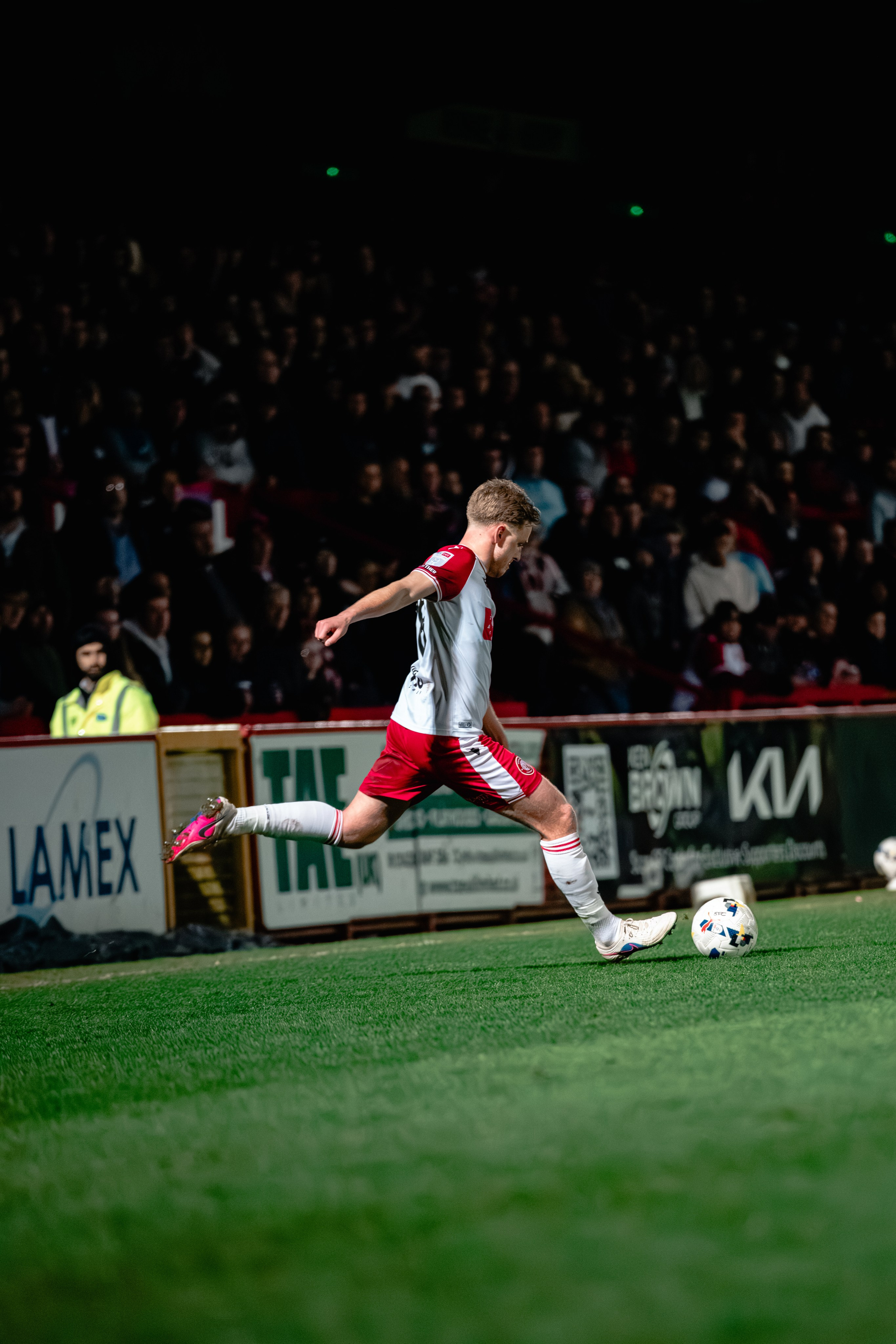 Stevenage player striking the ball during the League One fixture against Leyton Orient under the floodlights.
