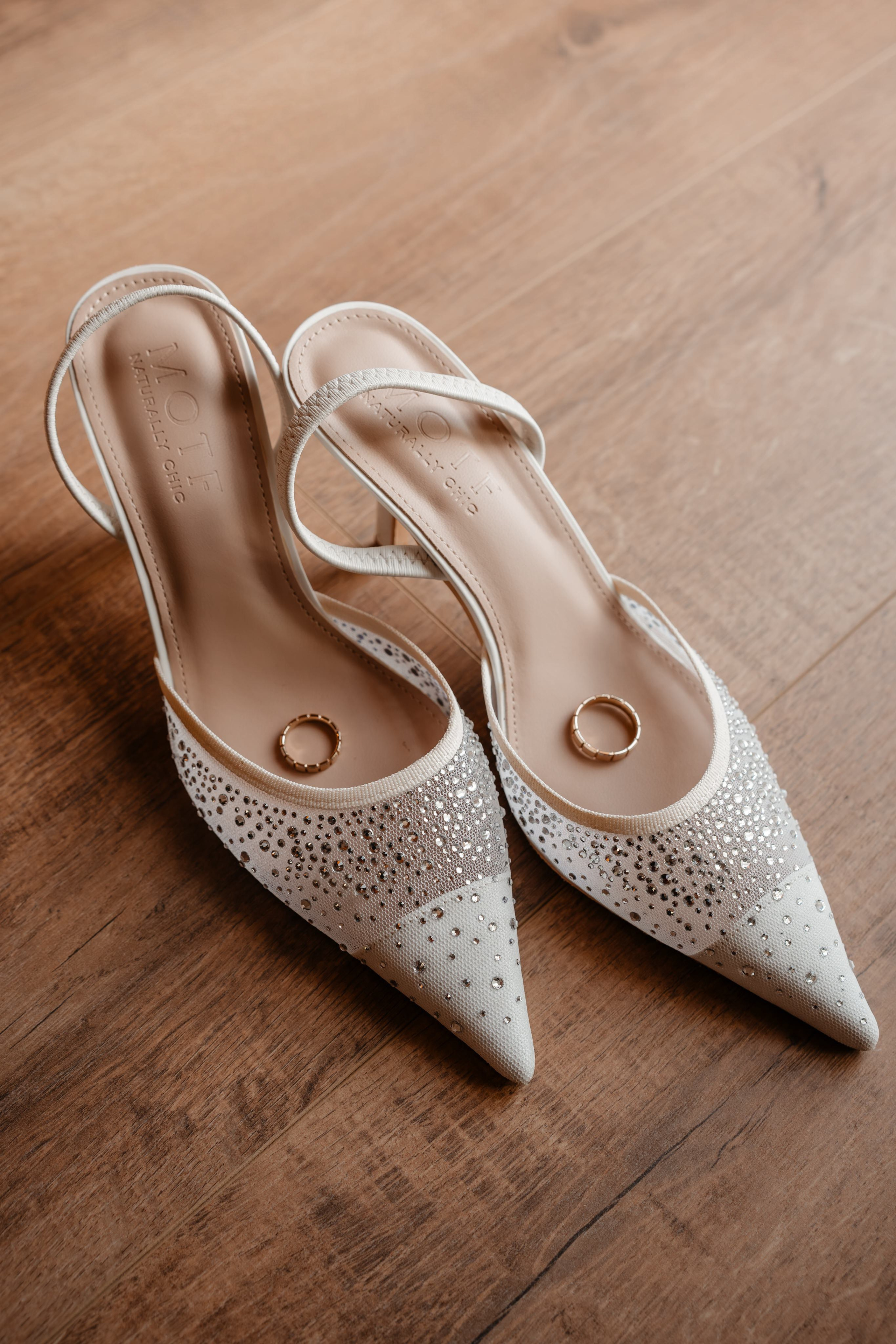 Pantofi eleganți de mireasă cu detalii strălucitoare pe parchet de lemn.
