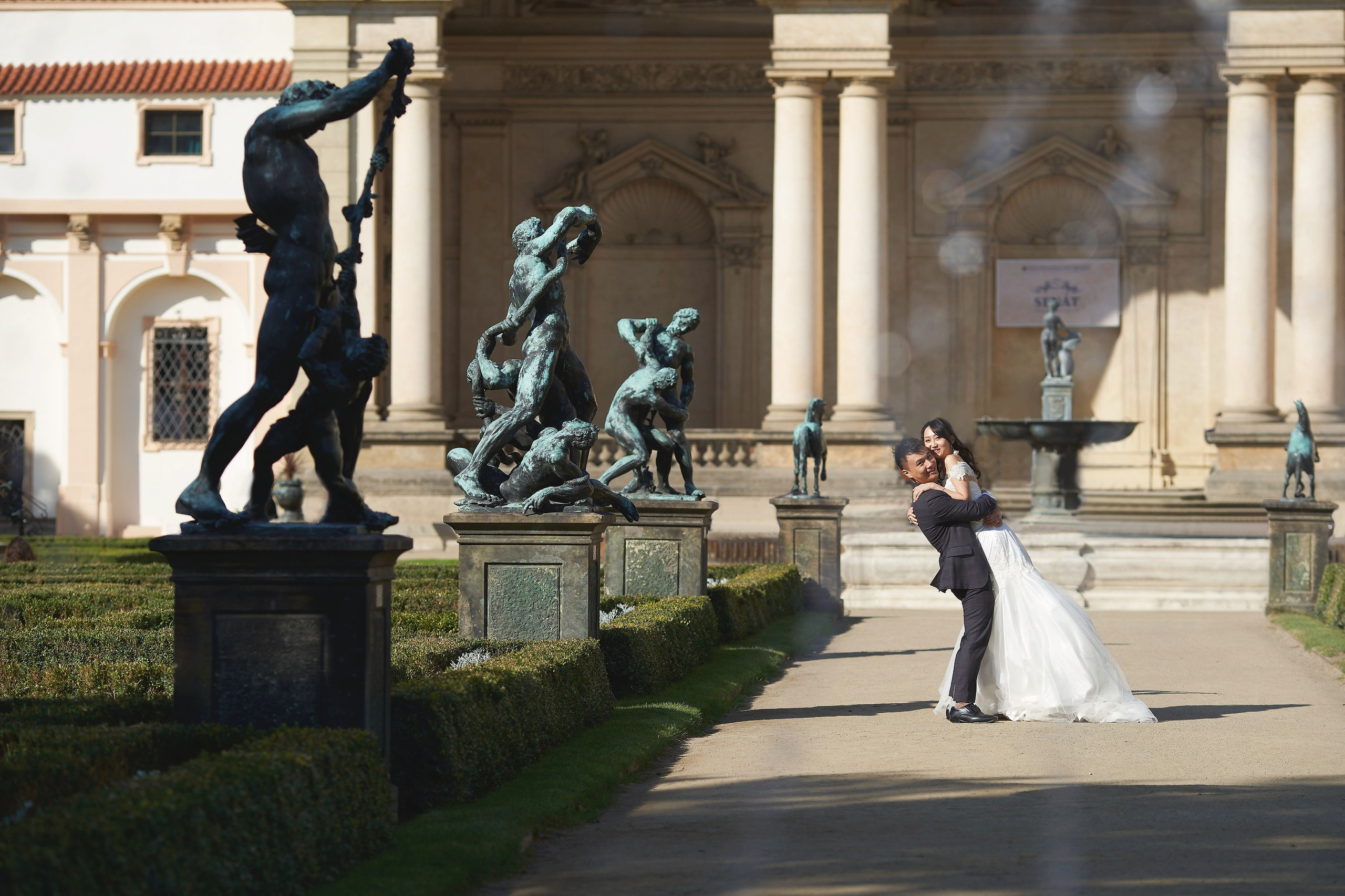 Groom Conan lifting bride Eva along the statue walkway in Wallenstein Garden.