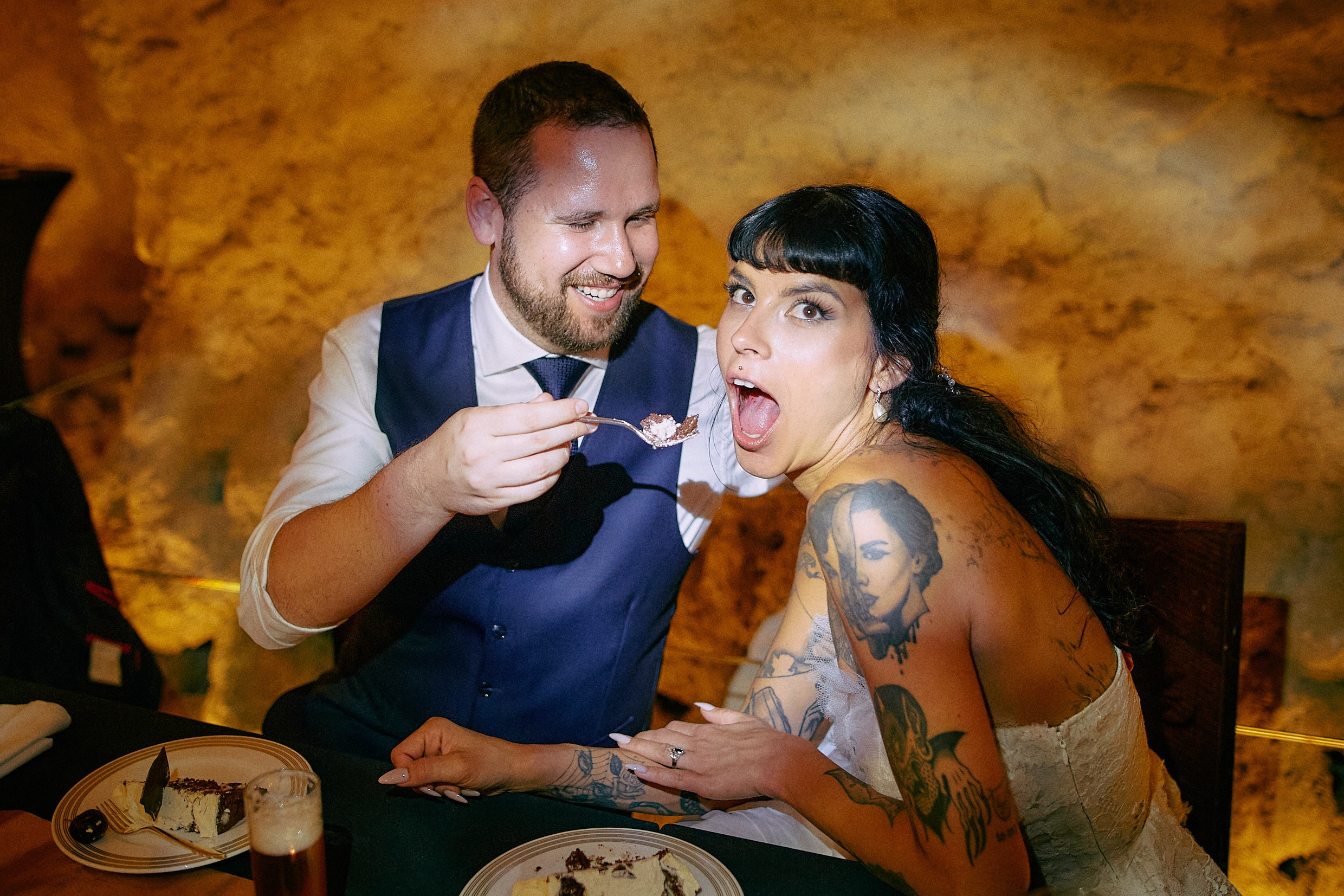 Bride feeding taking cake bite with laughing groom beside.