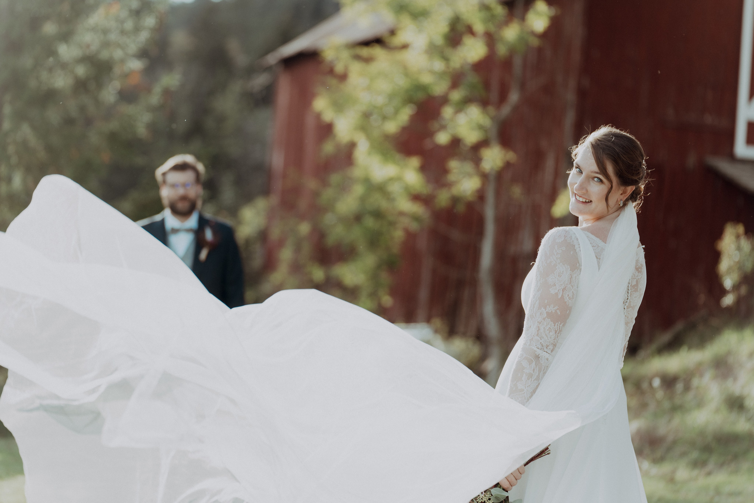 Brudens slør flagrer i vinden. Brudgommen står litt bak og ser på bruden