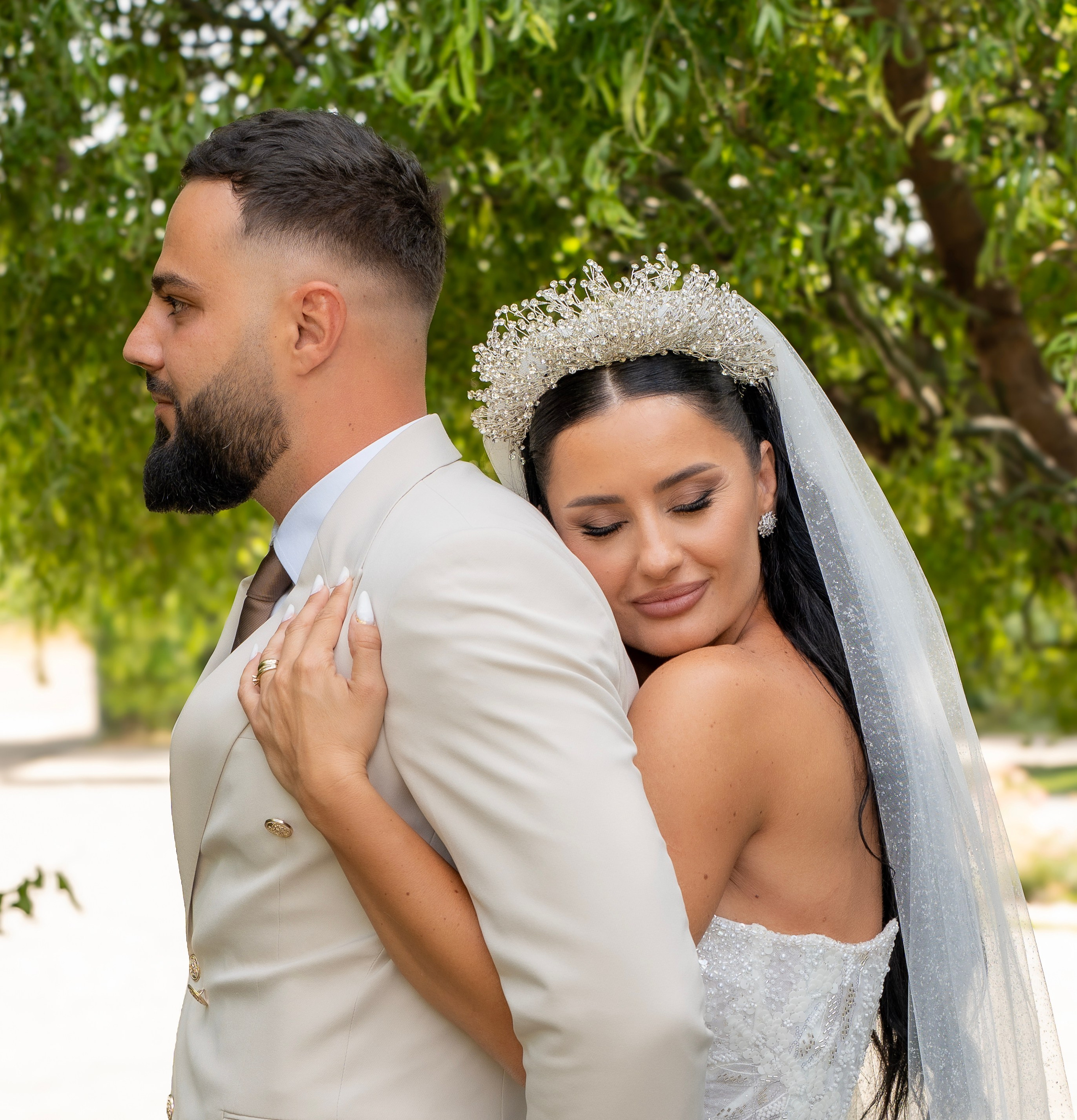 Bride and groom holding hands during wedding ceremony, both wearing crowns. Bride holds a bouquet of white flowers.